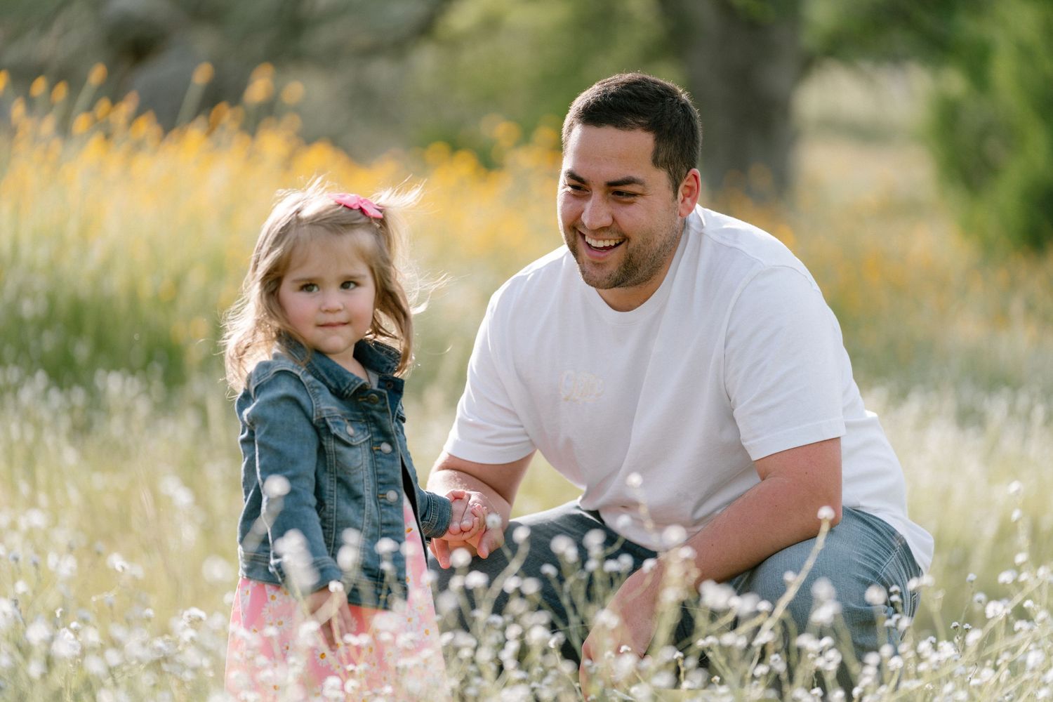 Playful family interaction in a meadow filled with white wildflowers.