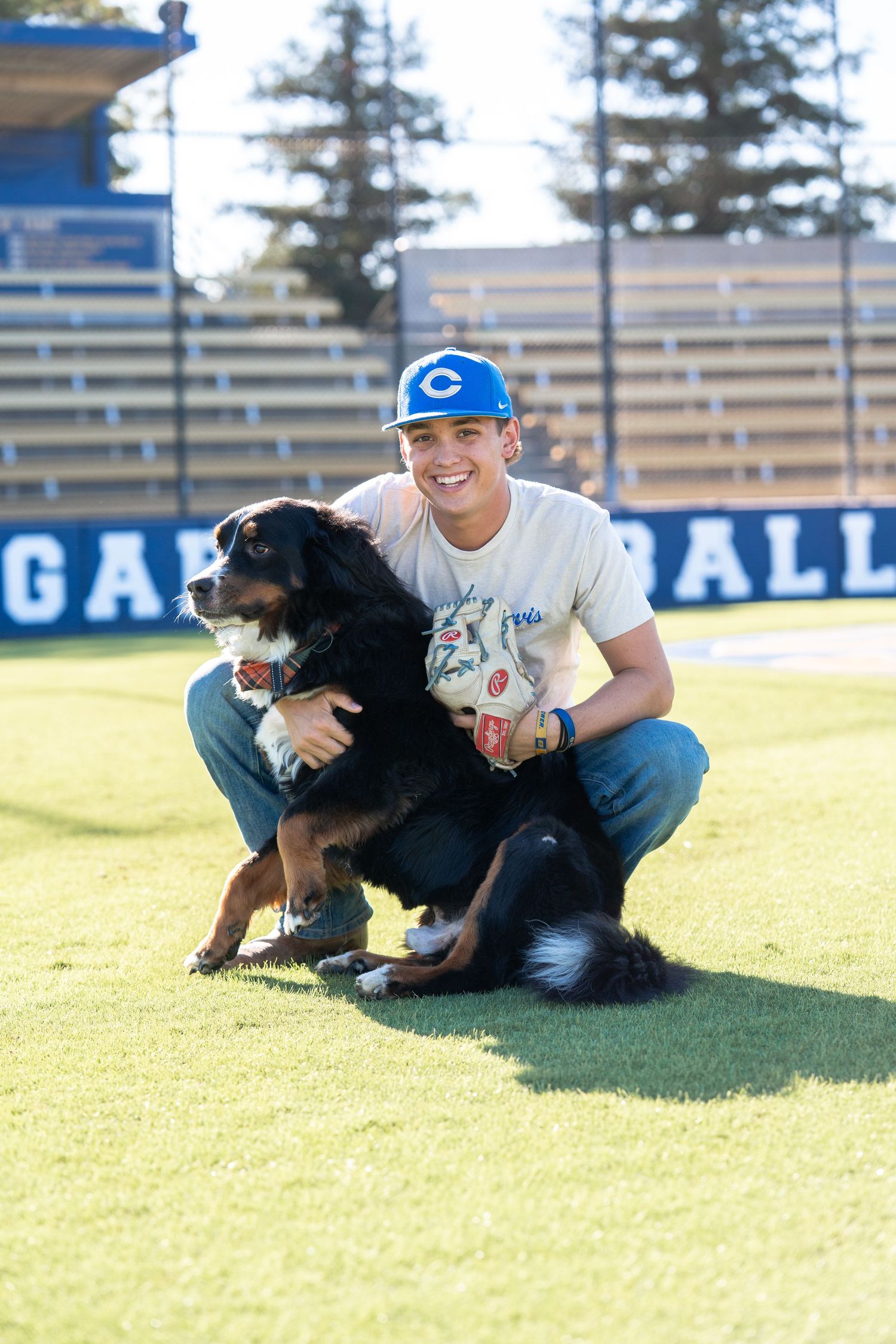 Playful moment with a black dog on a sports field with bleachers in the background.