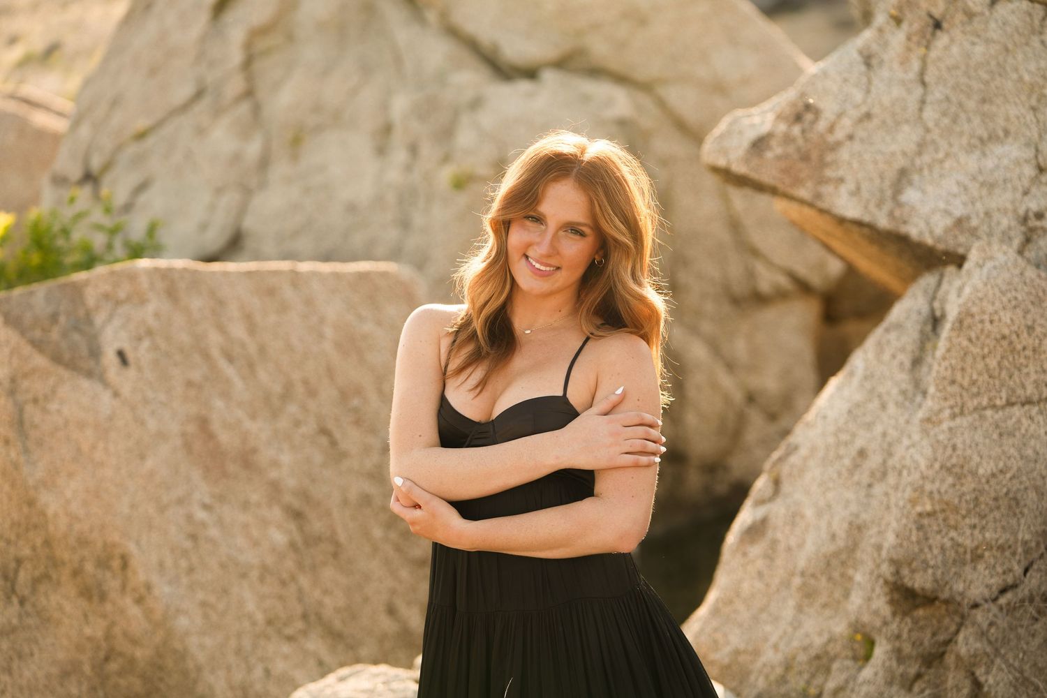 High School Senior  in black dress poses against rocky backdrop during golden hour photoshoot.