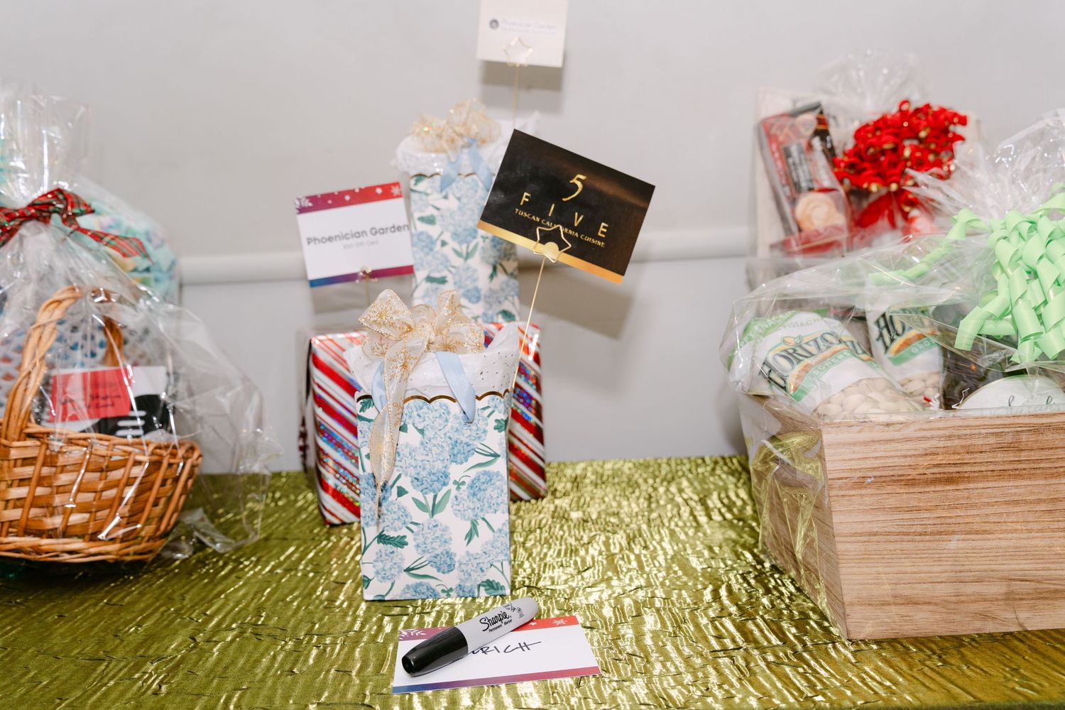 Gift baskets filled with holiday treats and decorations arranged on a shiny gold surface with festive ribbons and bows.