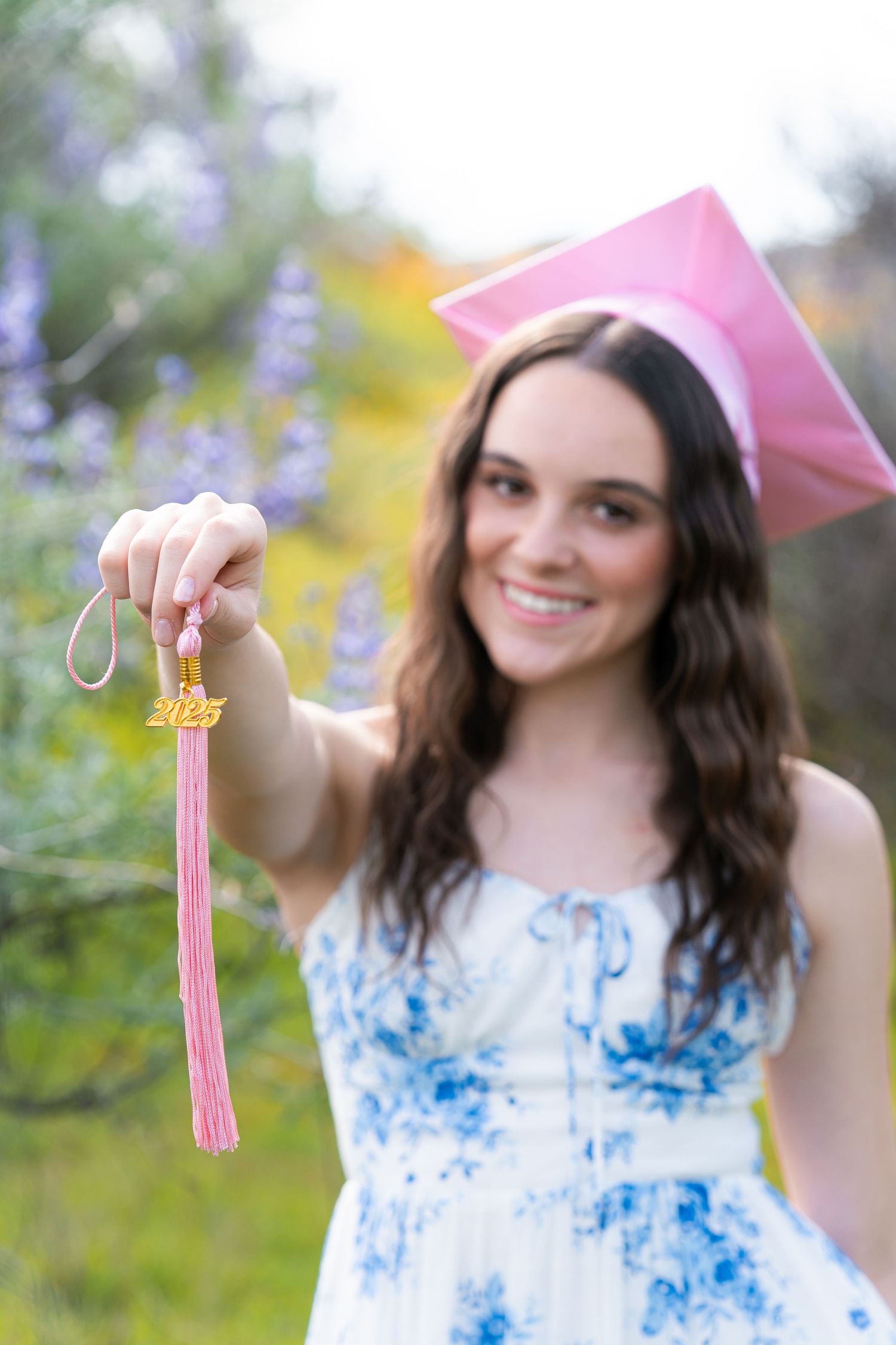 Graduate holding pink tassel with colorful wildflowers in background.