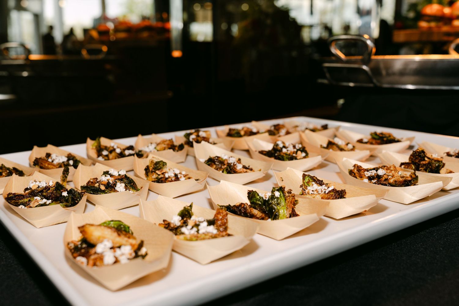 Elegant appetizers arranged on small wooden boats displayed on white serving platter.