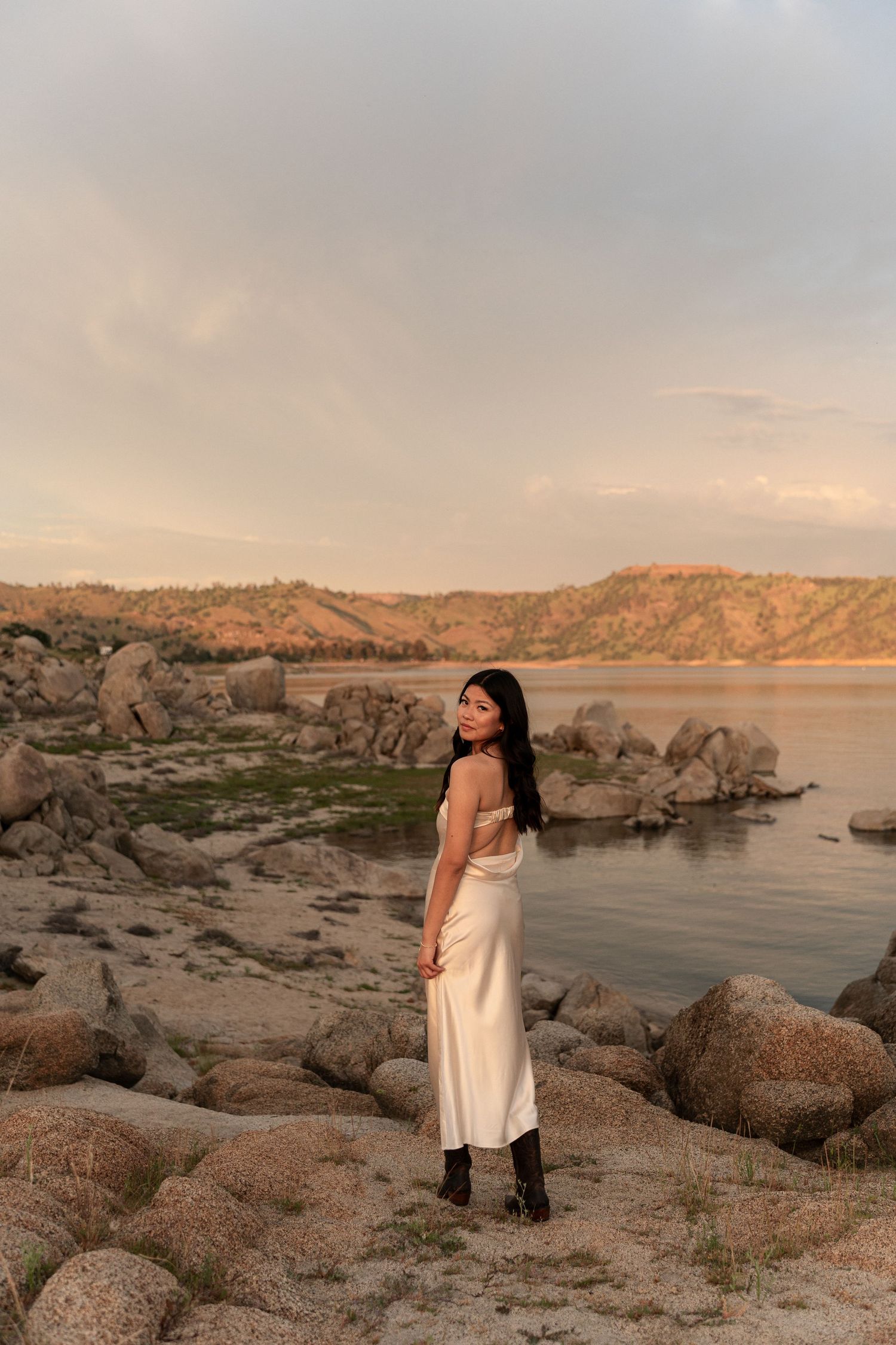 Scenic sunset photoshoot at a rocky lakeside with warm golden light reflecting off the water.