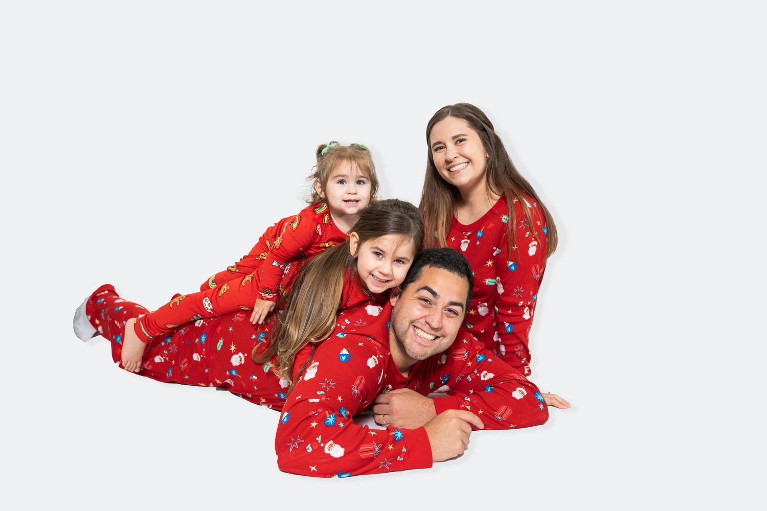 Family wearing matching red holiday pajamas poses together on white background.