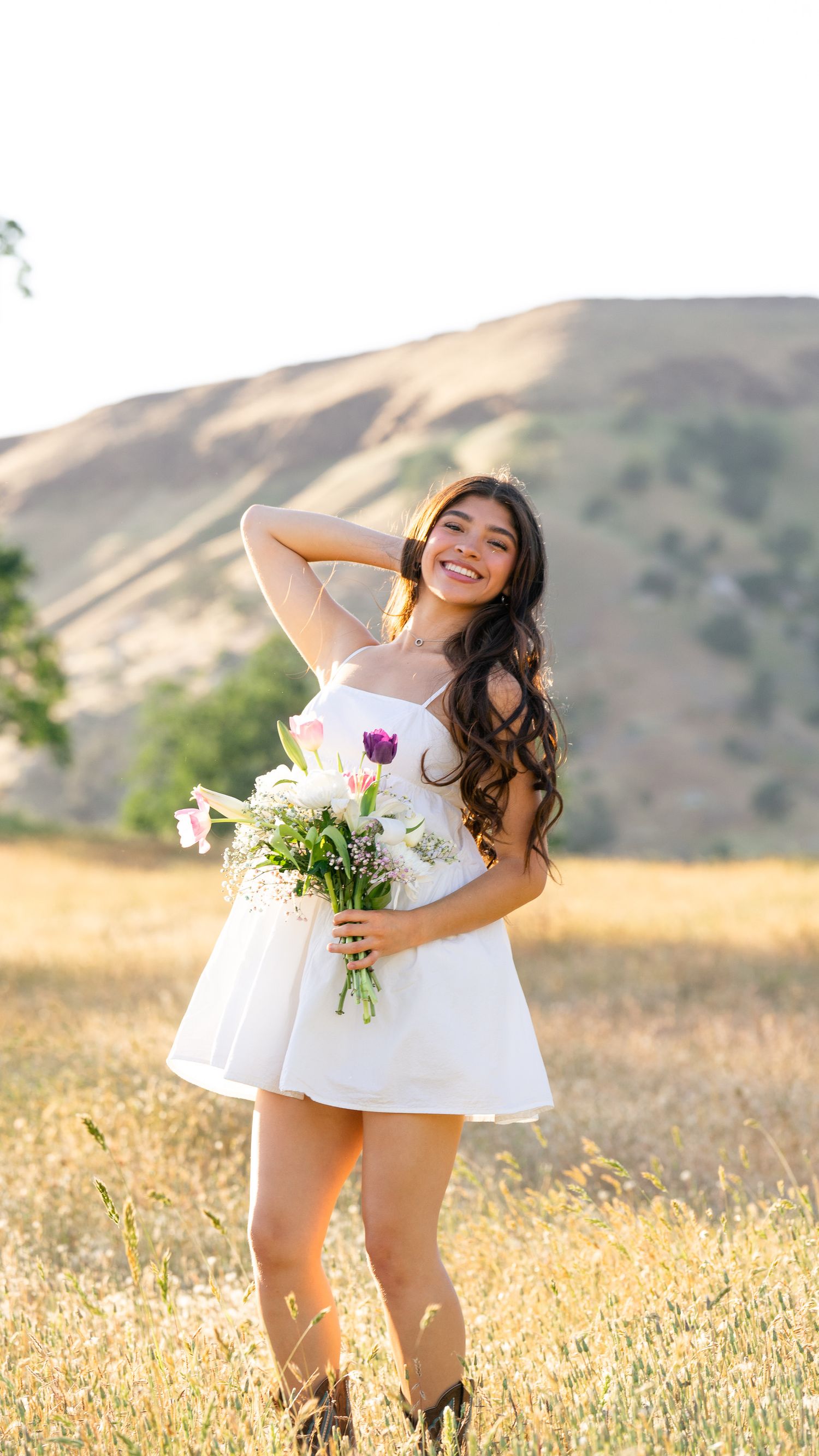 A person in a white dress twirls joyfully in a golden field at sunset with mountains in the background.