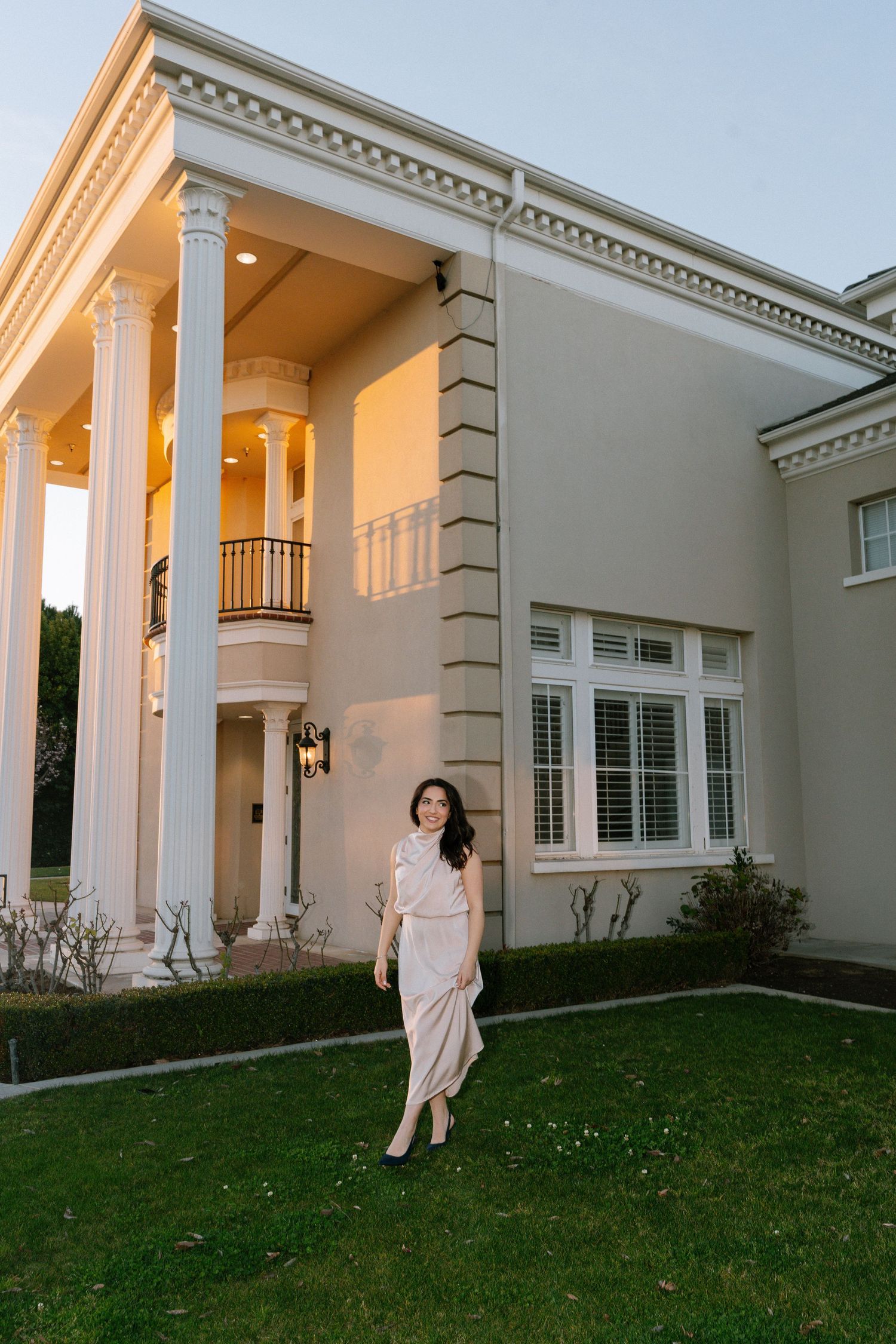 Elegant white mansion exterior with columns and grassy lawn captured during golden hour lighting.