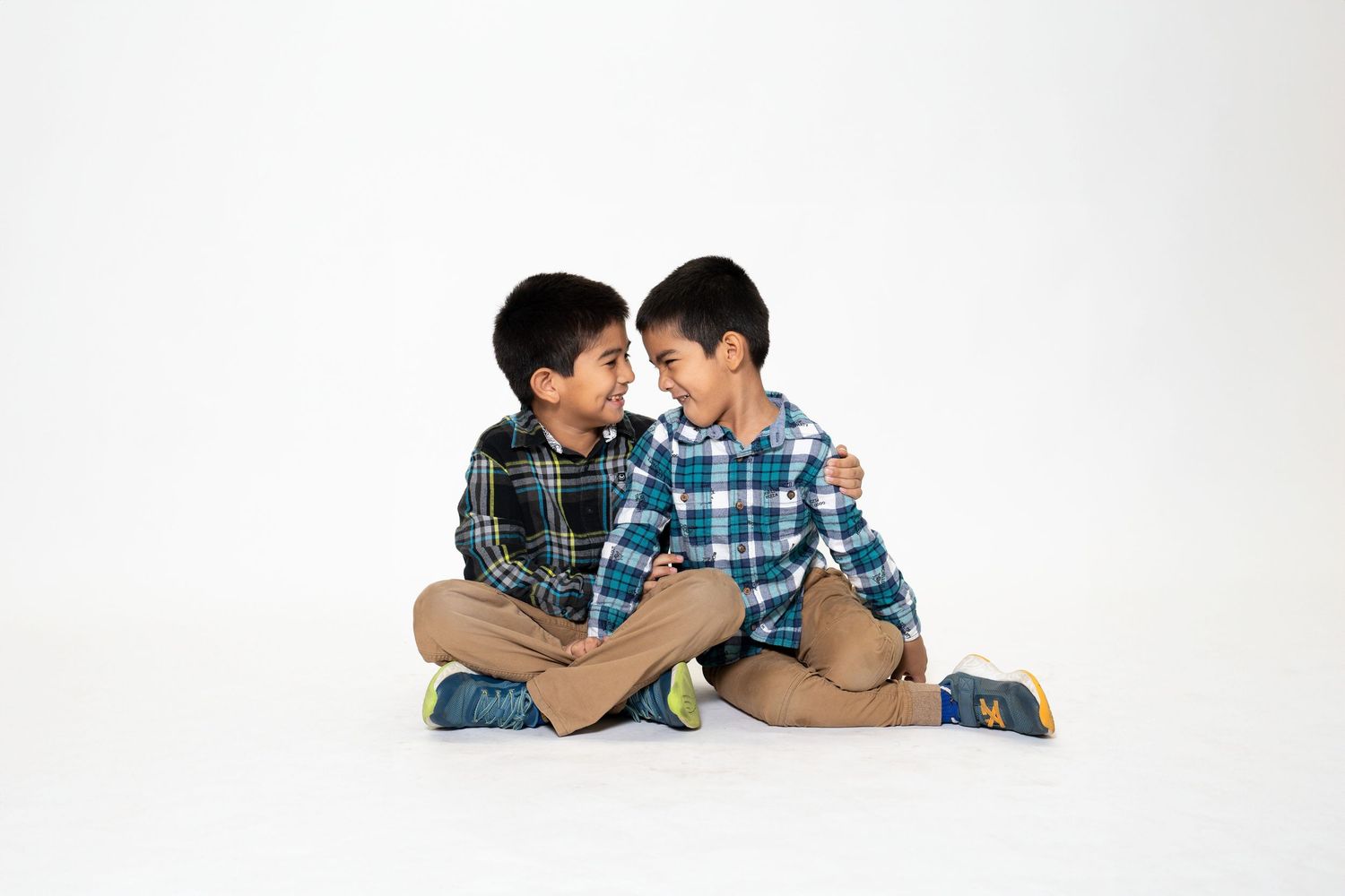 Two young boys in plaid shirts sitting together on white background.