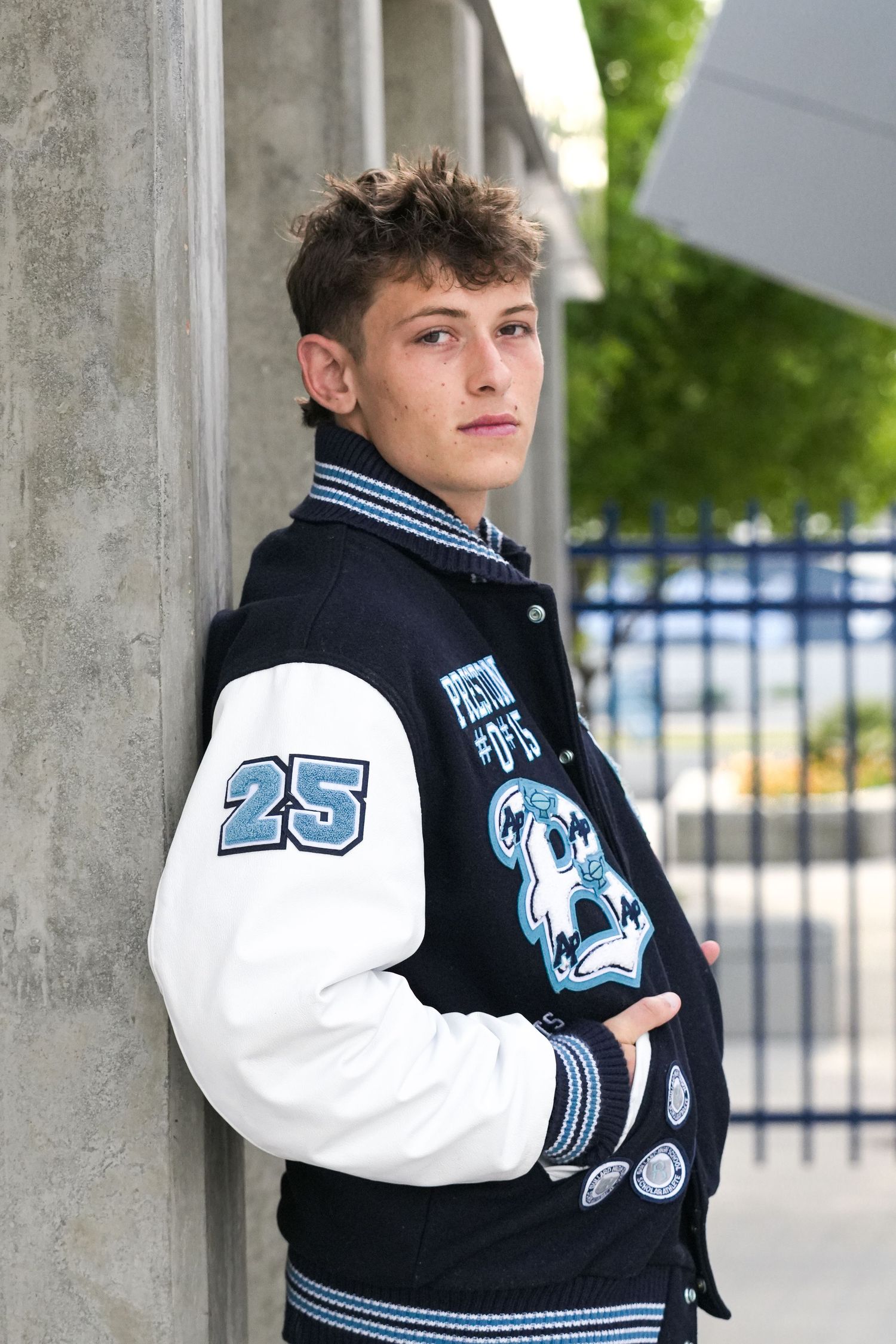 Athletic varsity jacket with number 25 shown in stylized outdoor portrait series.