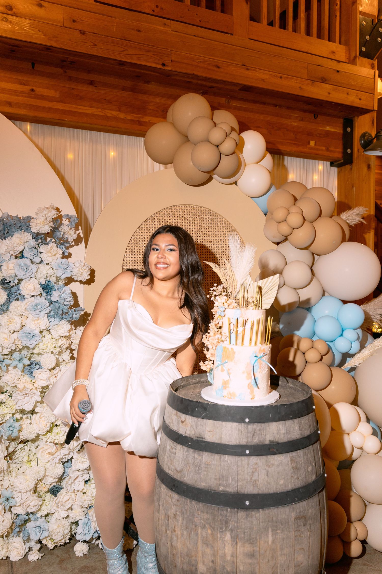 Celebratory scene with white and blue balloon arch, wooden barrel decor, and floral arrangements at an elegant party.