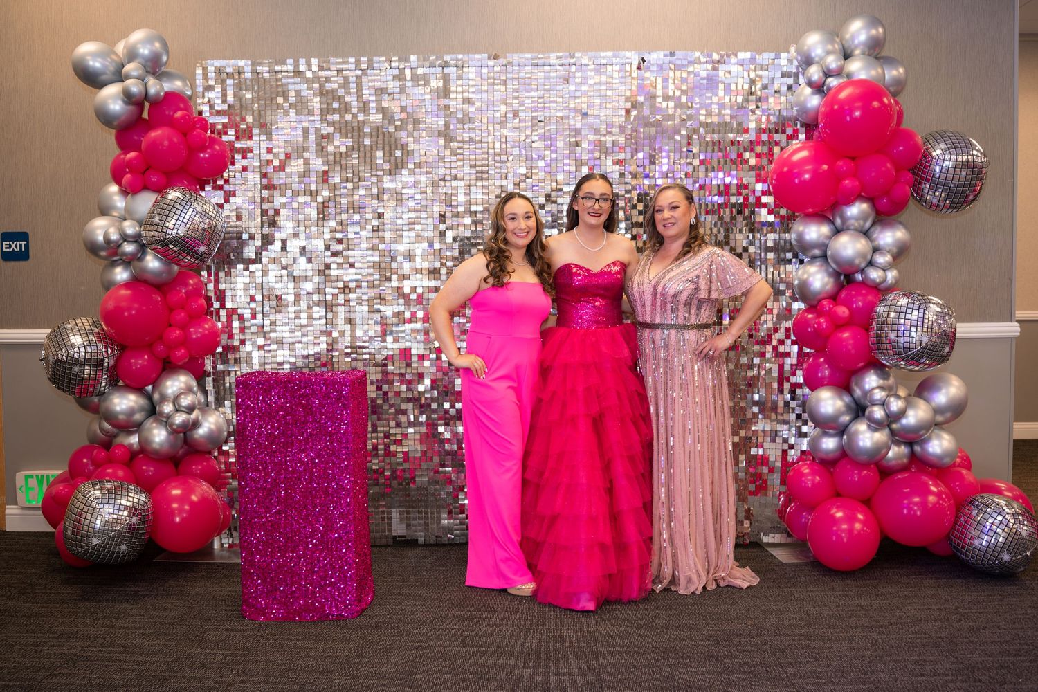 Sparkly silver backdrop with pink balloon arrangements and floral decor creates festive party atmosphere.