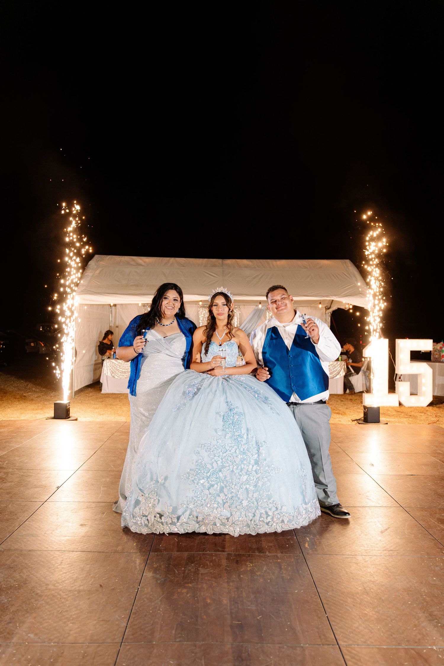 A quinceañera celebration with sparklers and illuminated number 15 display at night.