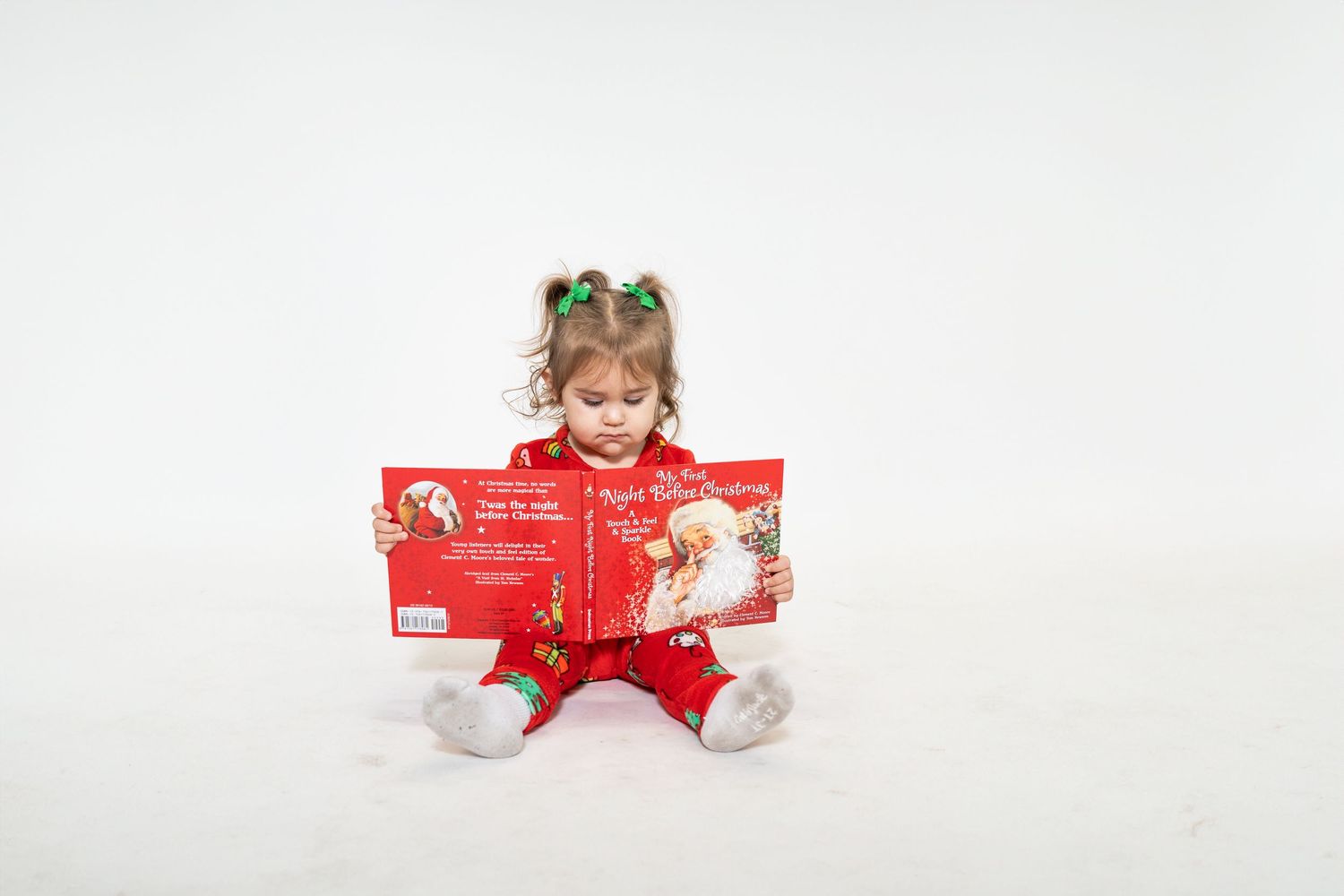 Young child in red pajamas reads holiday book while sitting in studio setting