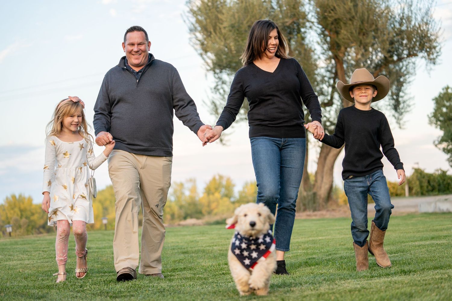 A family walks together on grass with their dog during a sunny afternoon.