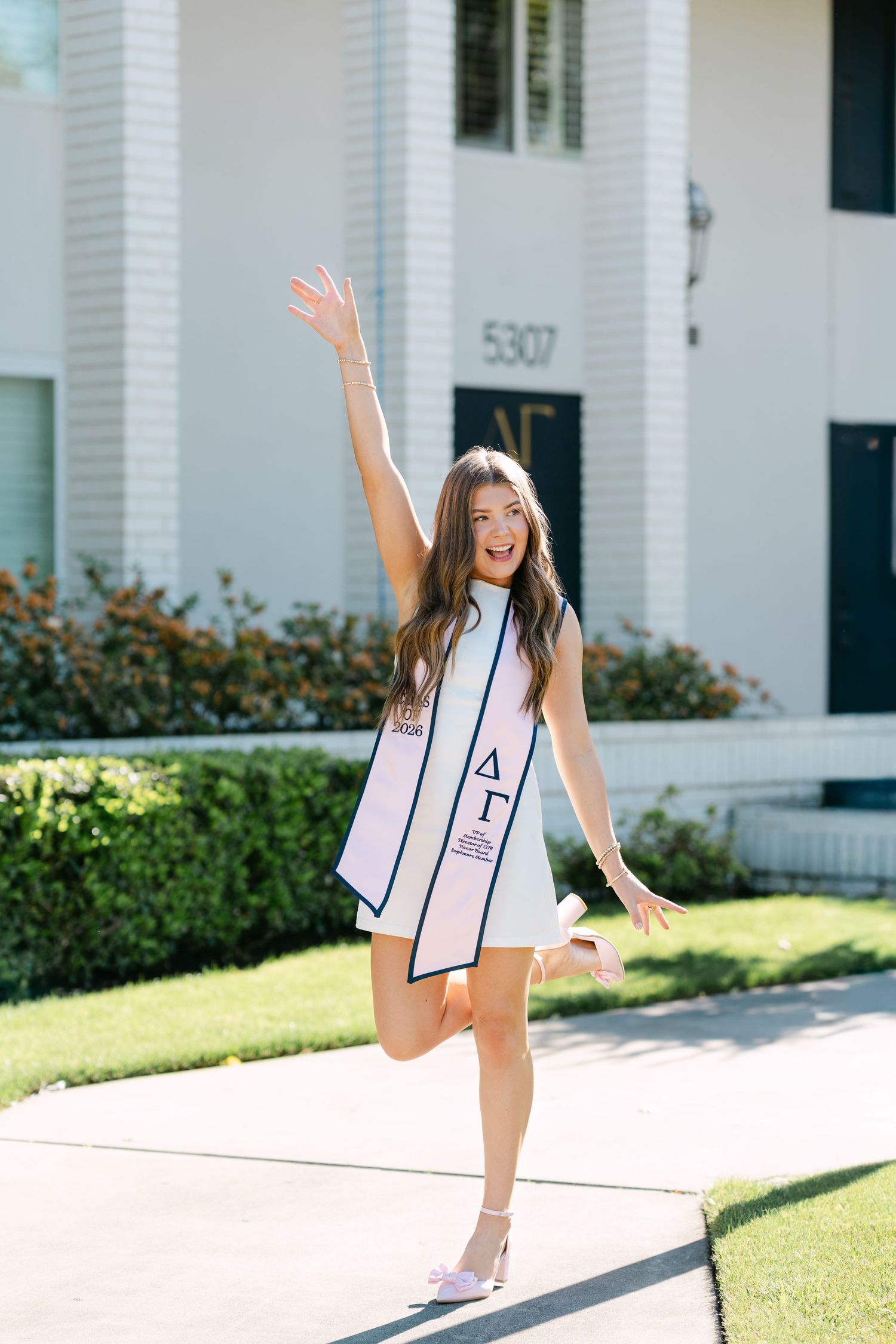 Young woman in white Delta Gamma sorority stole posing joyfully on sidewalk outside chapter house numbered 5307.
