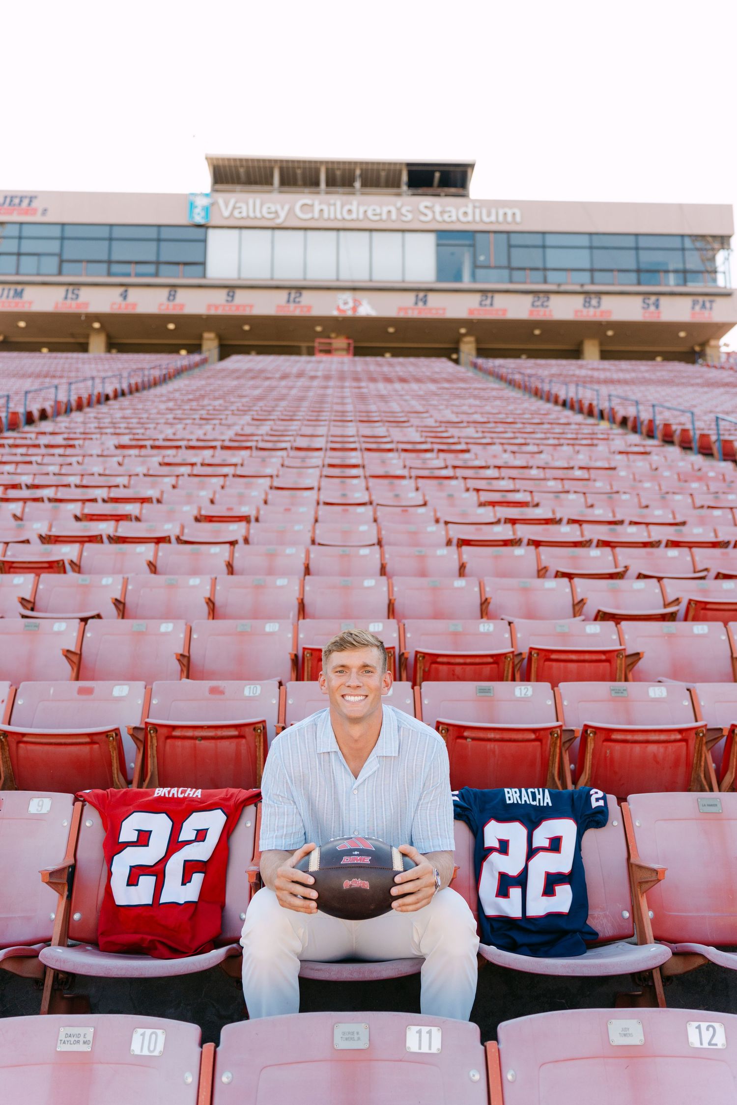 Young man smiling in stadium seats at Valley Children's Stadium holding football with two #22 jerseys beside him.