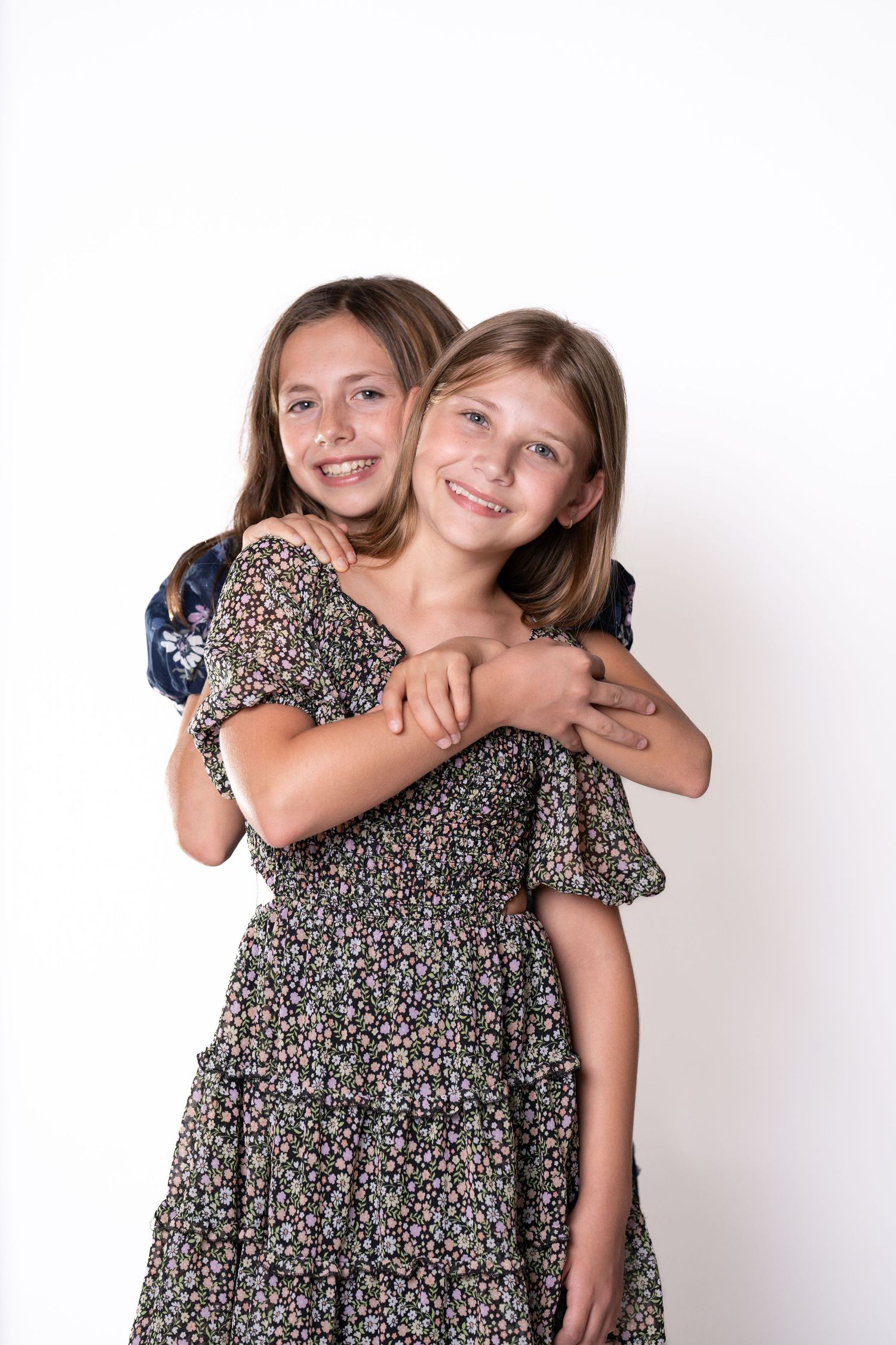Two people in floral dresses posing playfully against white background.