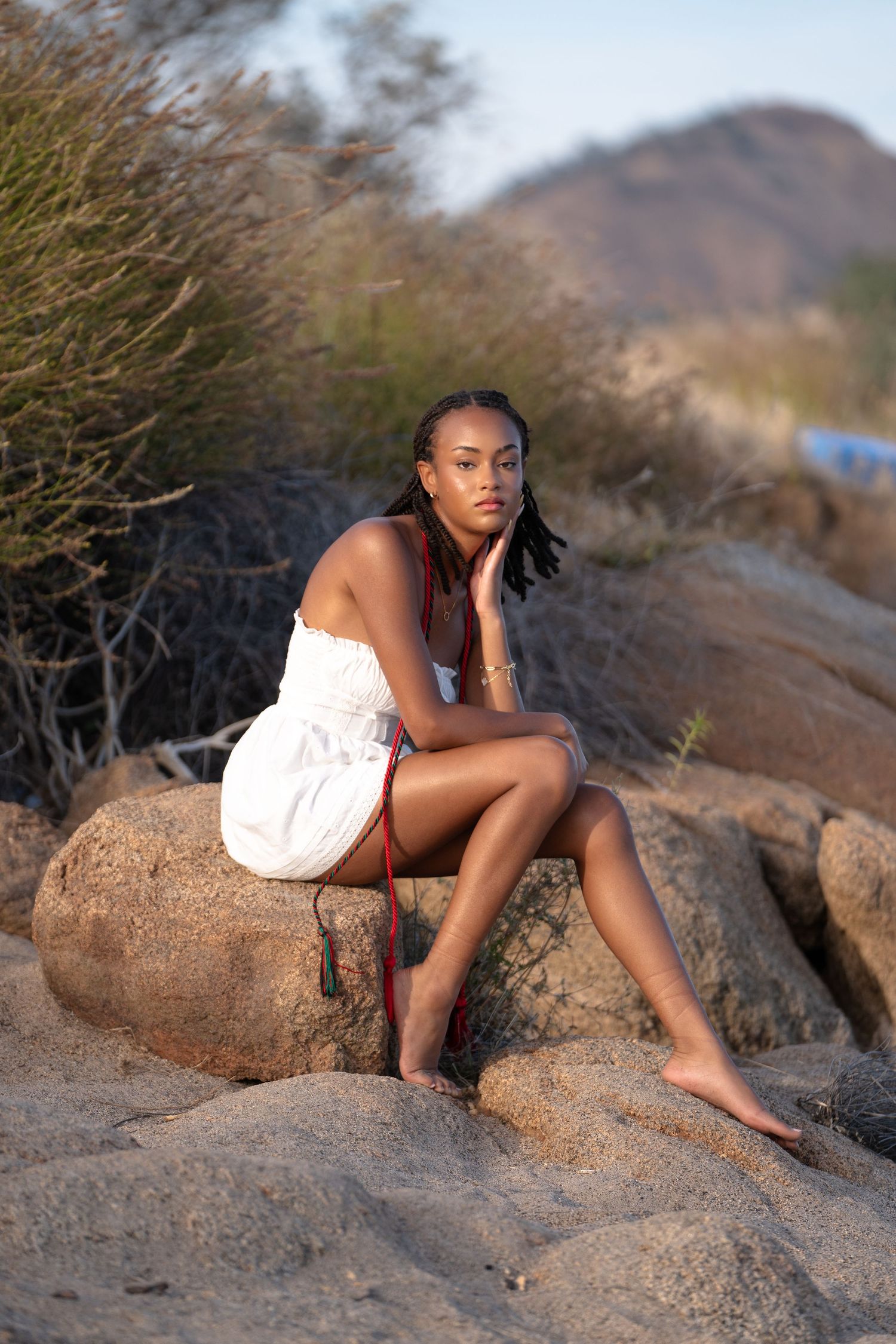 Person in white dress poses on rocky terrain with mountains in background.