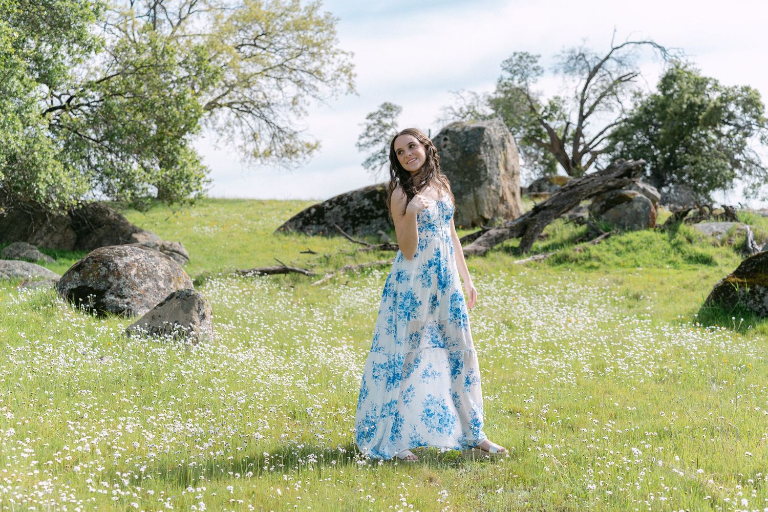Artistic photoshoot in a sunny meadow with green grass and scattered wildflowers.