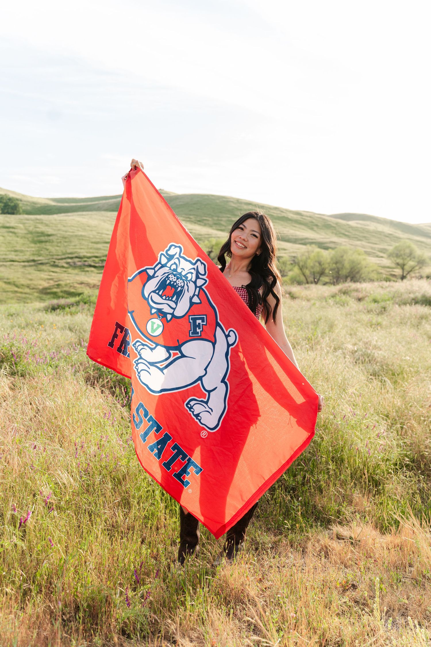 Person holding red school spirit flag with bulldog mascot in grassy field.