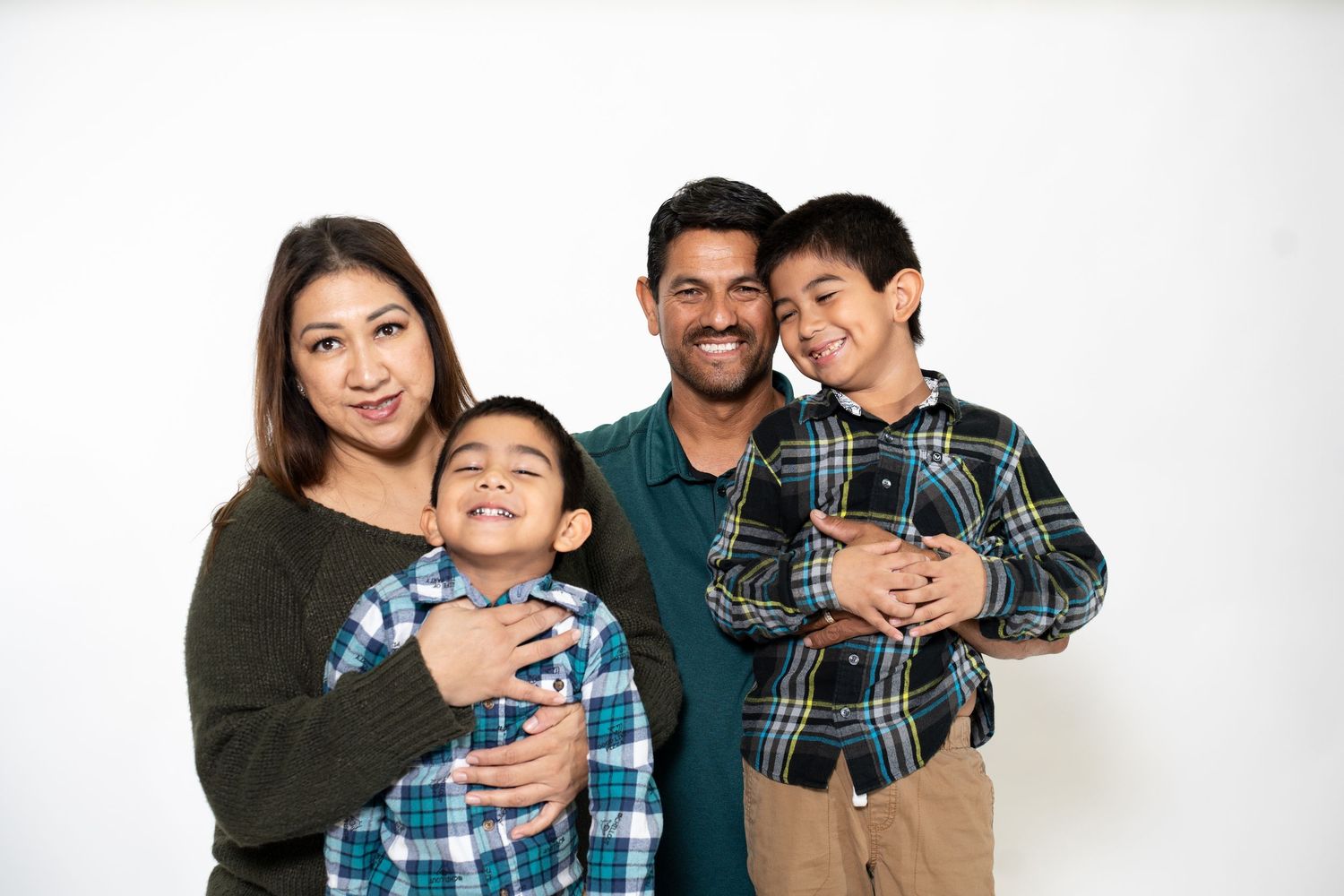 Happy family of four poses together against white background in casual attire.