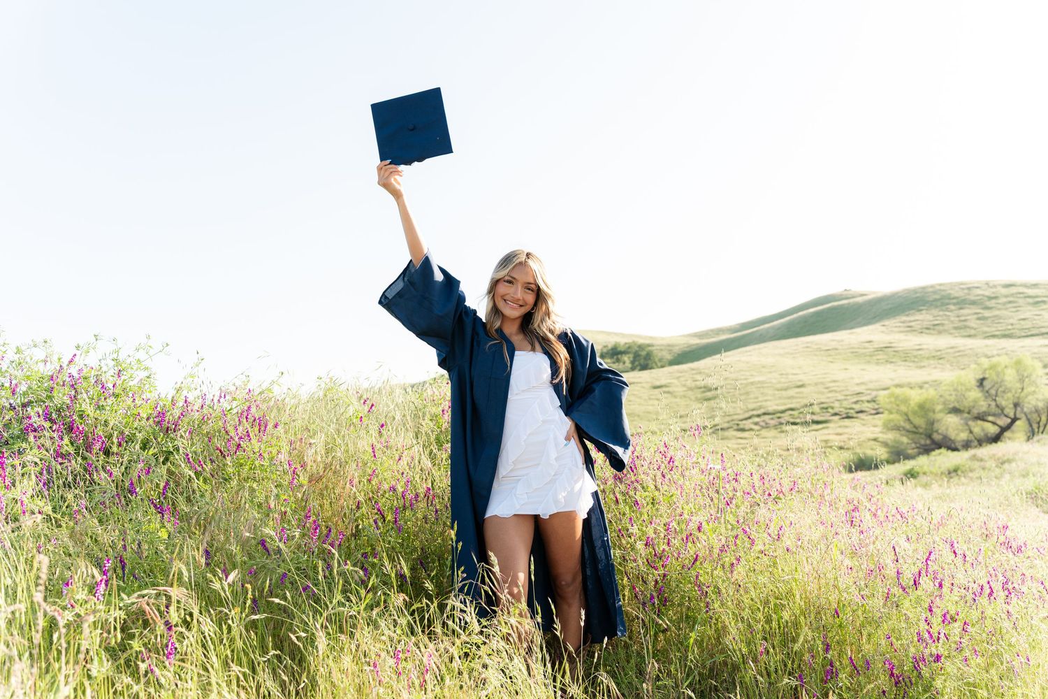 Graduate celebrating in a scenic field of wildflowers at sunset.