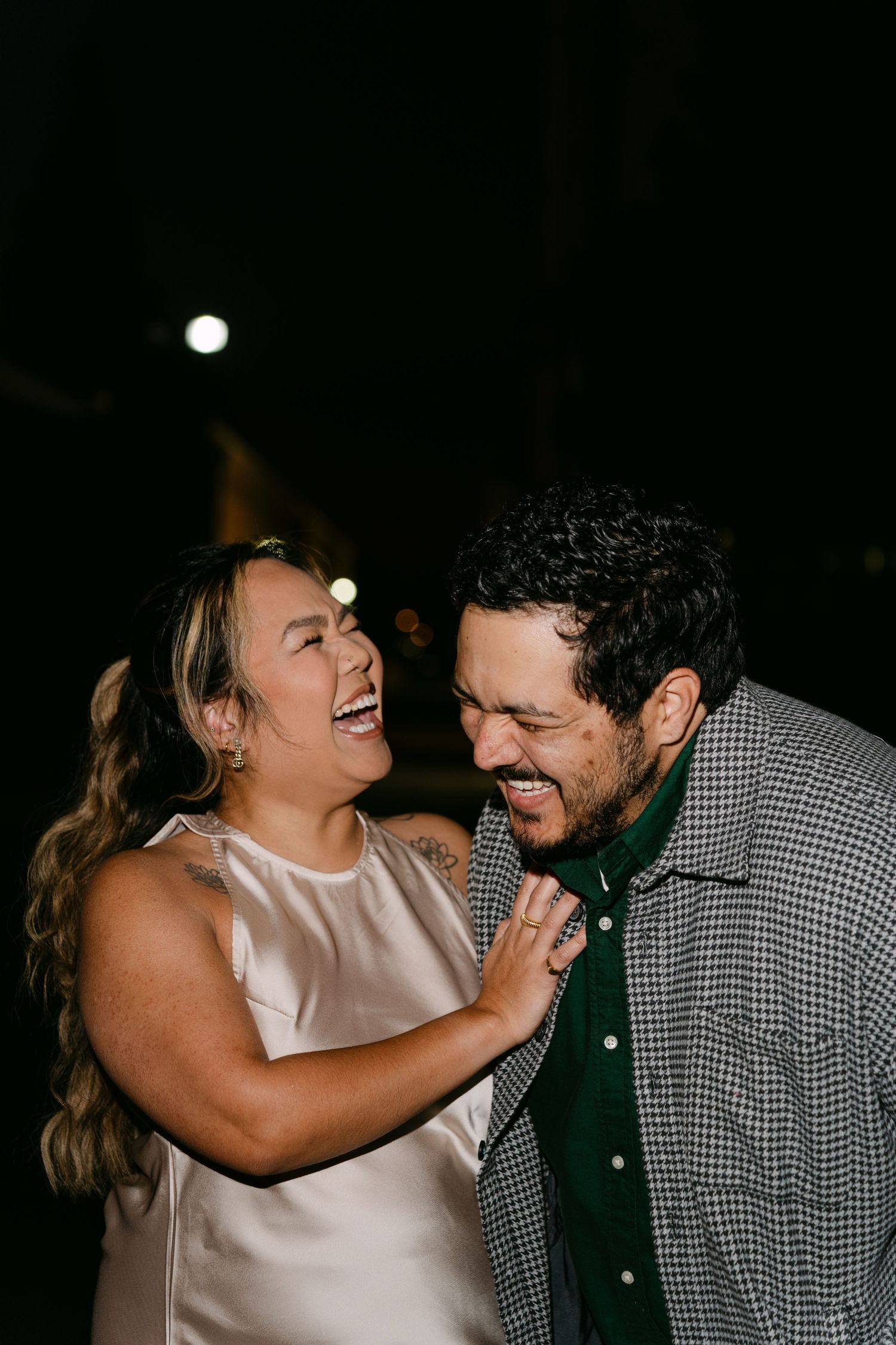 A couple shares joyful laughter while dancing together in a dimly lit setting.