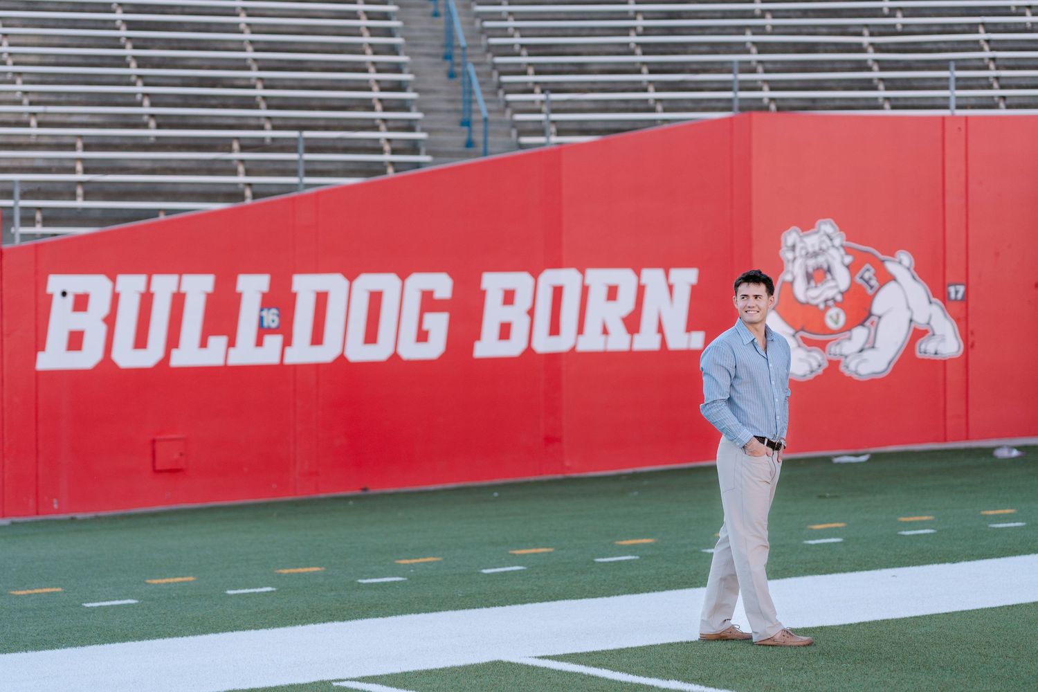 Young man standing in front of a red Bulldog Born wall mural at Fresno State football stadium.