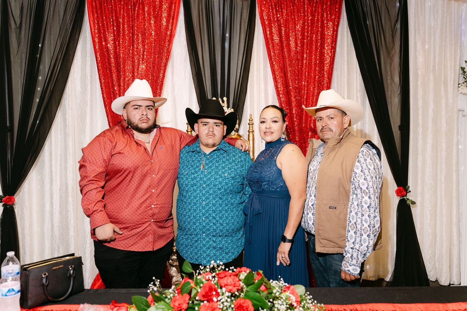 Group of people posing in front of black and red curtains at a photo booth event.