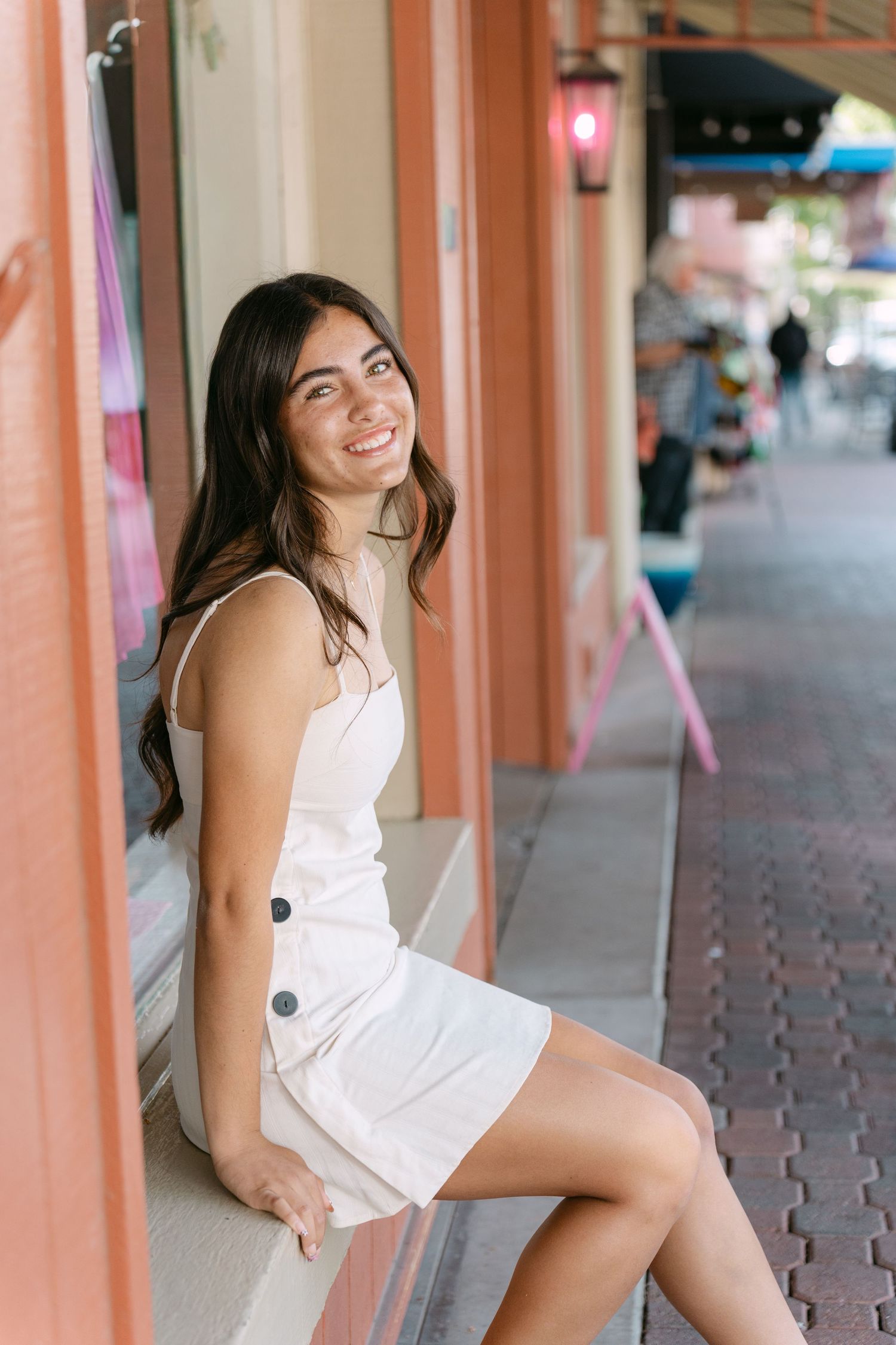 A series of photos showing someone in a white dress posing playfully against pink columns in an outdoor setting.