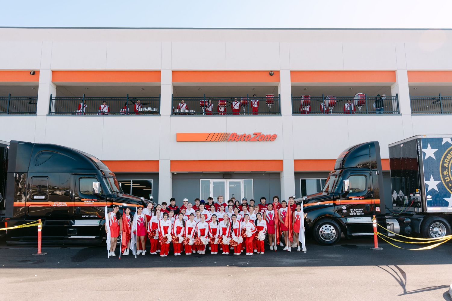 Wide shot of cheerleaders in red and white uniforms lined up for a group photo outside a commercial building.