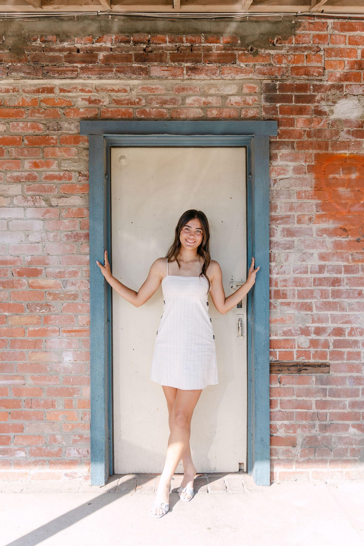 A series of five photos showing someone in a white dress posing within blue-framed doorways against a rustic brick wall.
