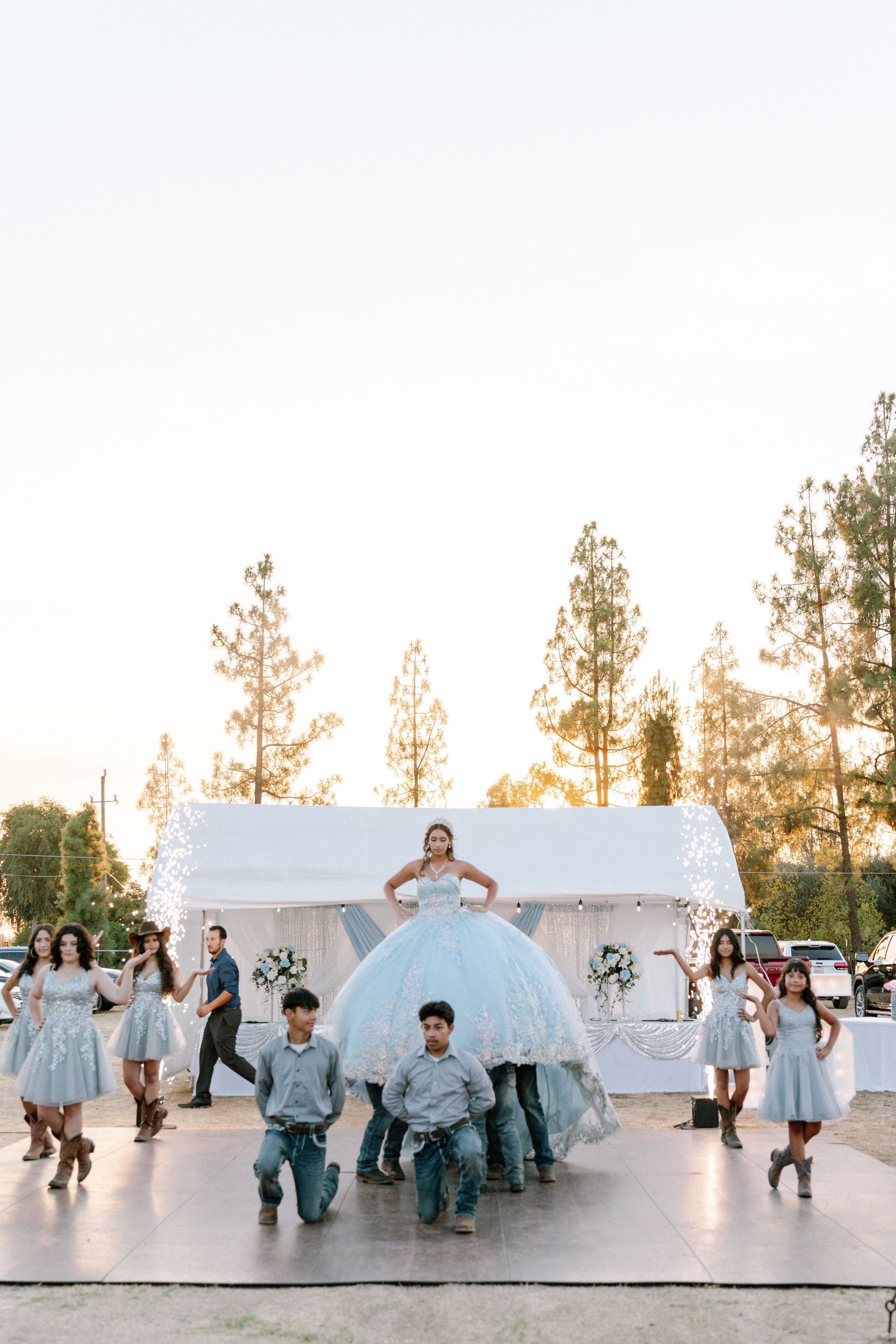 Wedding party dancing and jumping in light blue attire surrounded by fog on an outdoor dance floor.
