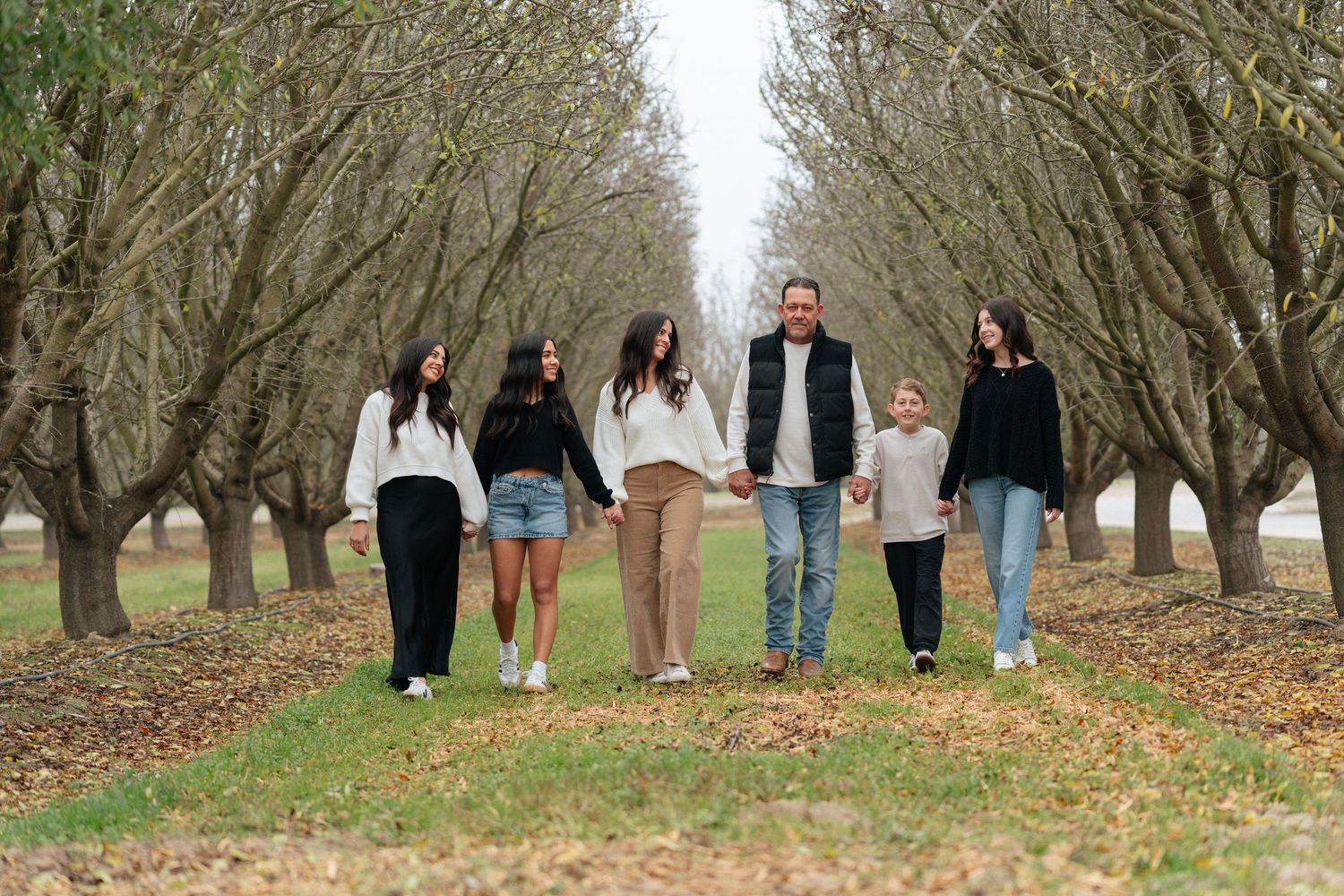 A group walks together down a tree-lined path covered in fallen autumn leaves.