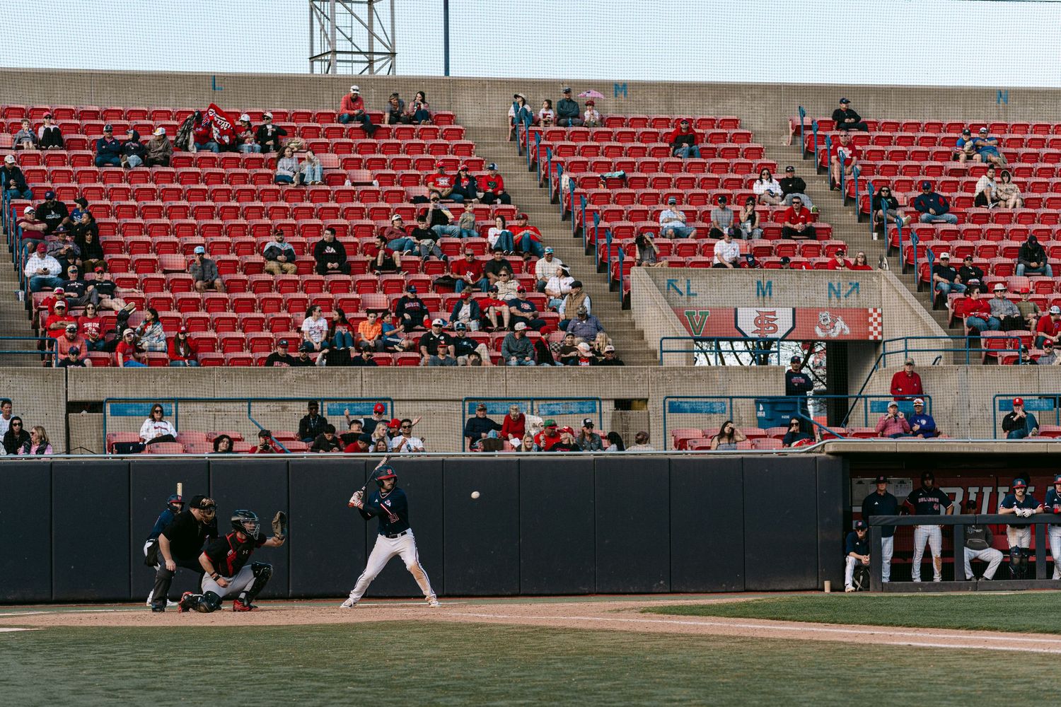 Baseball game in progress at a stadium with red seats and scattered spectators in the stands.