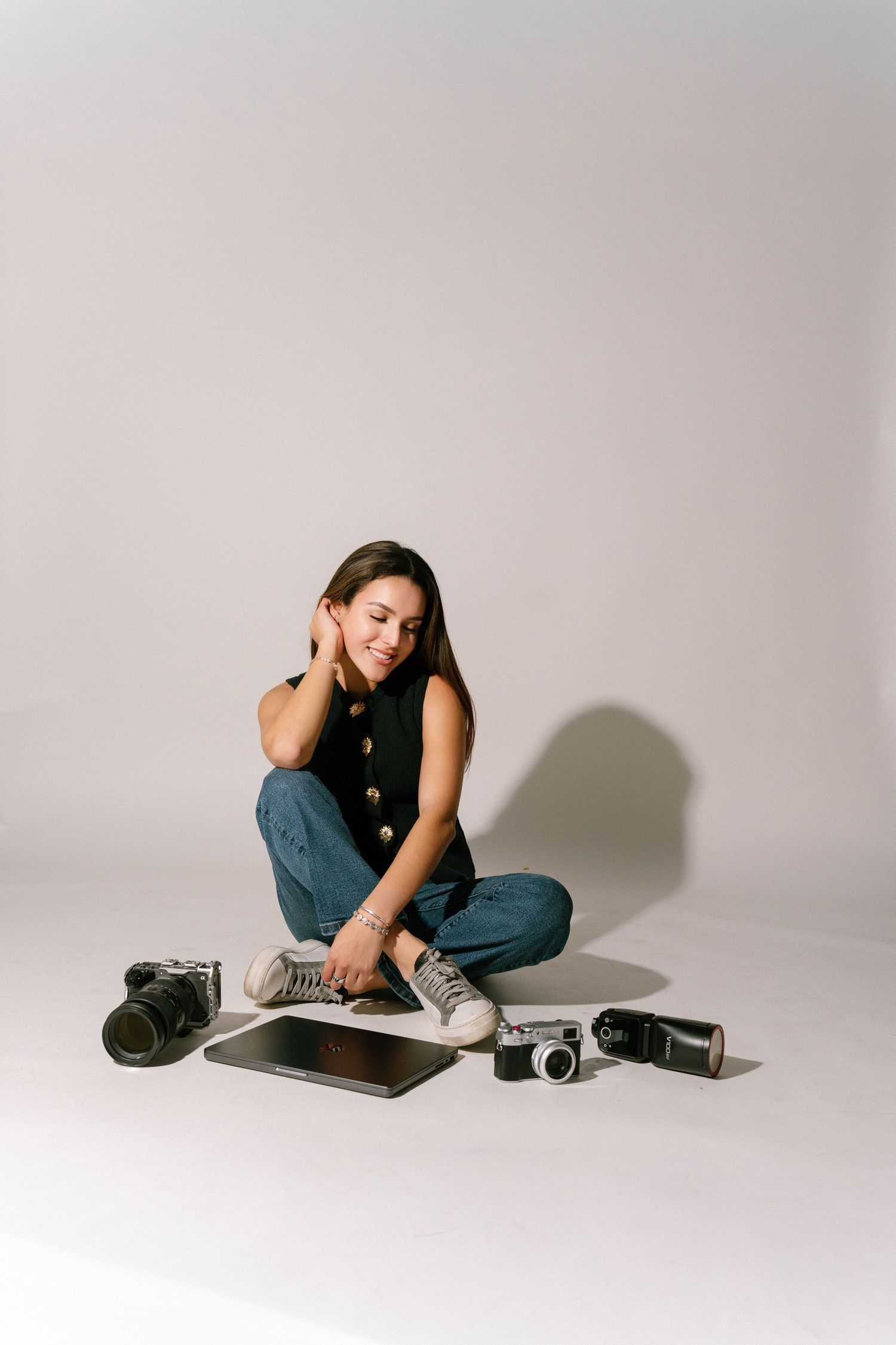 A series of minimalist studio portraits showing a person in casual attire posing on a white floor with vintage cameras nearby.