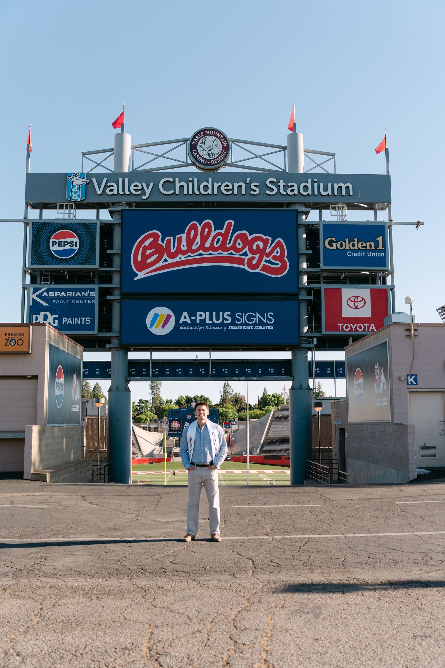 Man standing in front of Valley Children's Stadium Bulldogs scoreboard at Fresno State on a sunny day.