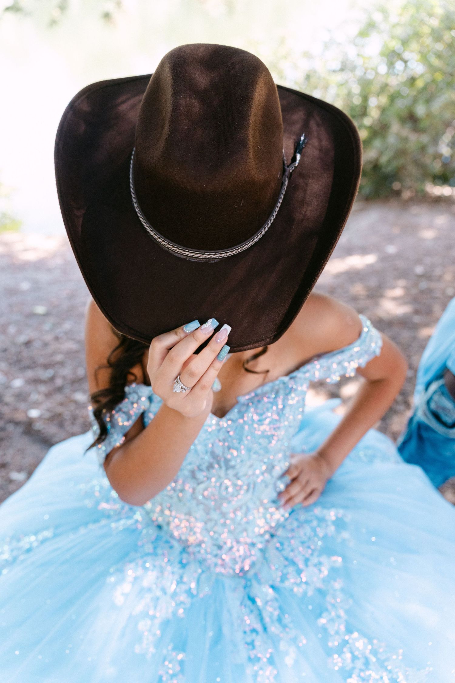 A person in a blue quinceañera dress and black cowboy hat poses for photos outdoors.