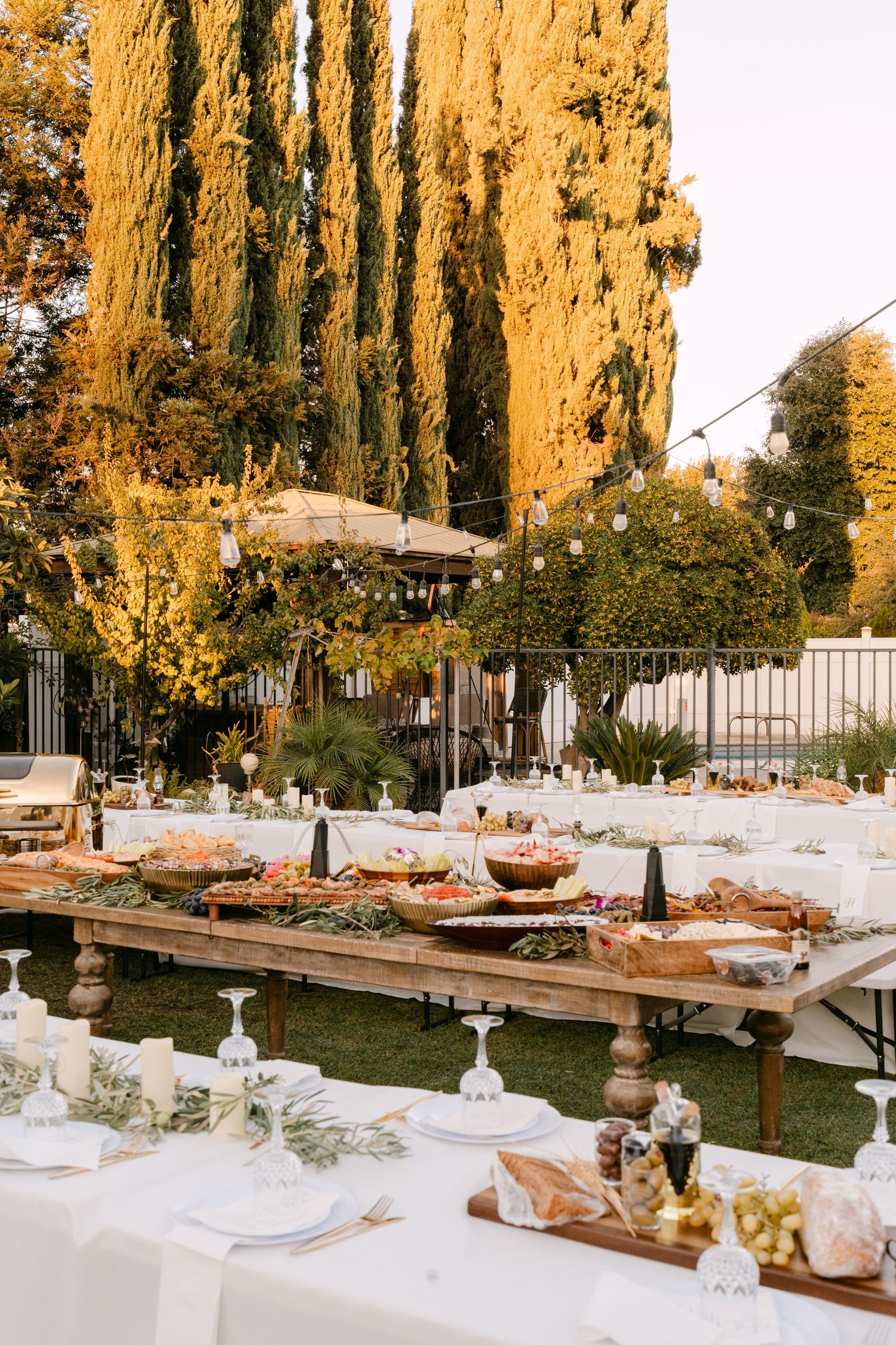 Outdoor wedding reception setup with long tables and cypress trees glowing in golden hour light.
