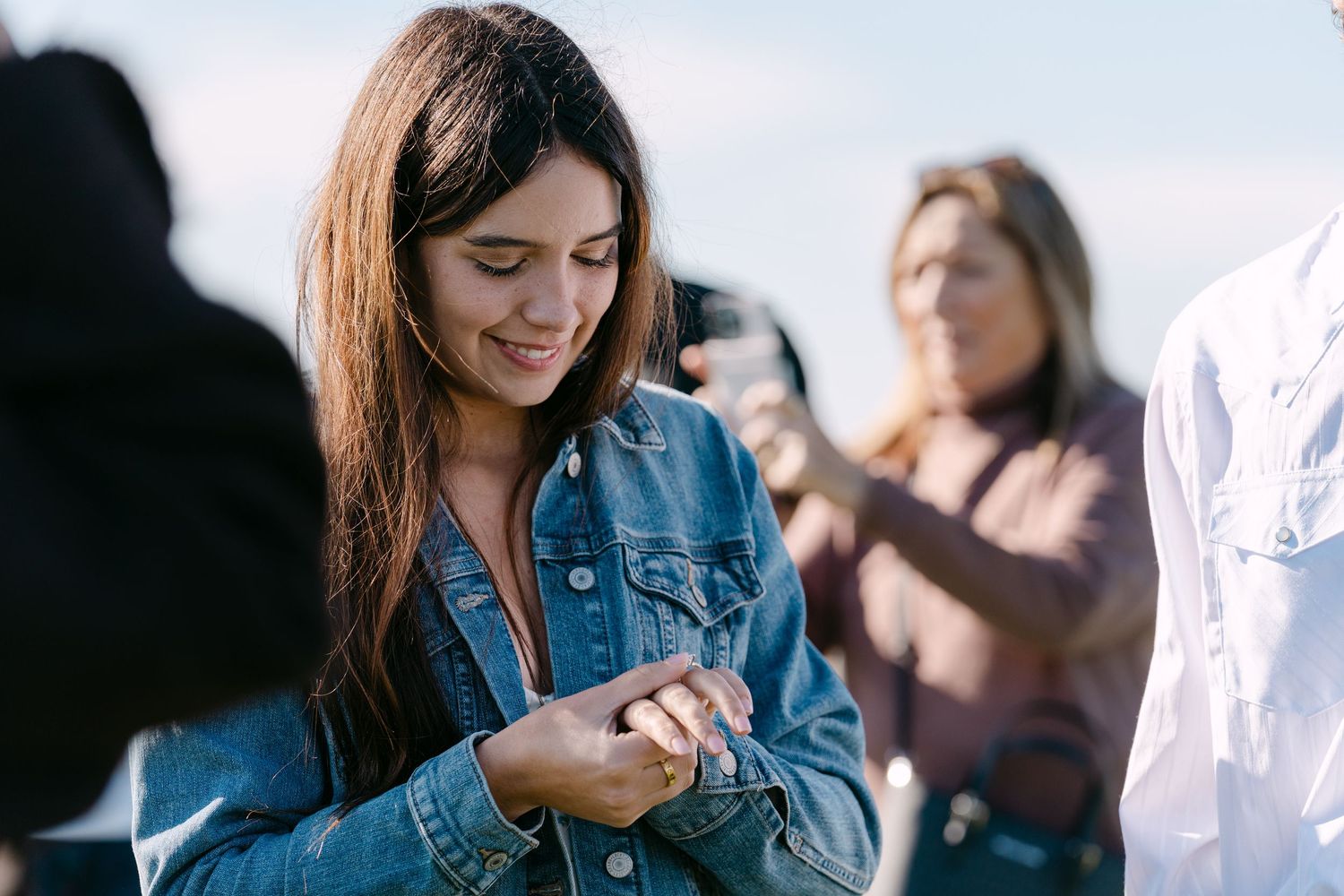 A person in a denim jacket stands outdoors in soft natural lighting while holding a smartphone.
