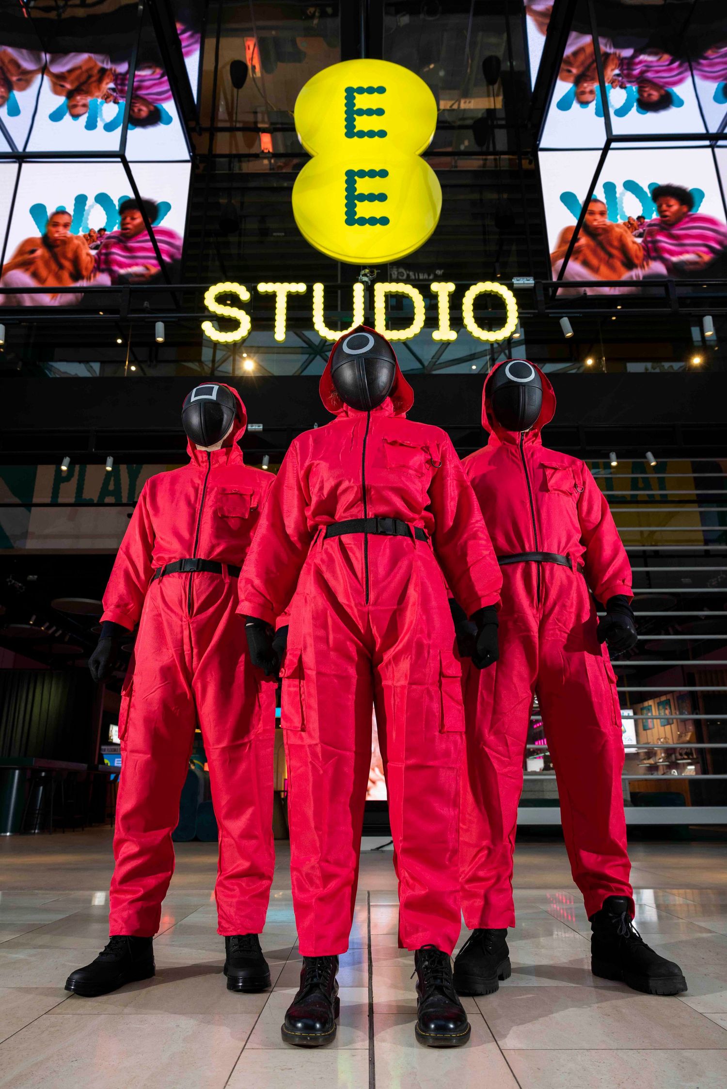 People in matching red coveralls lined up against dark background with studio signage. London Event Photographer