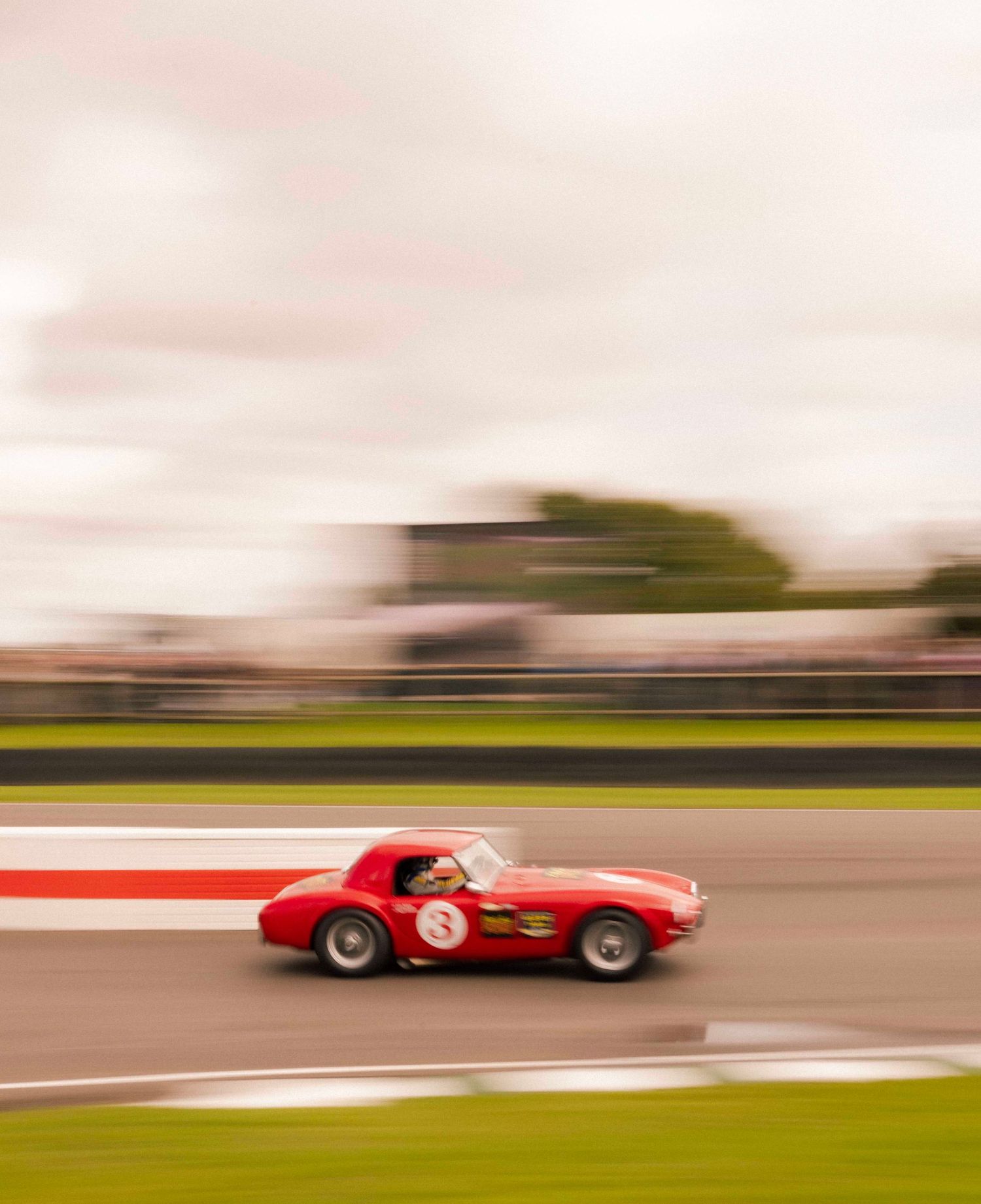 Motion-blurred red vintage racing car speeding past on a racetrack. London Event Photographer