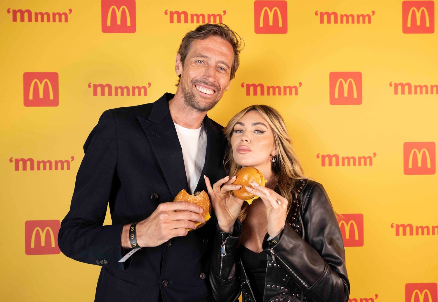 Two people posing with McDonald's burgers against yellow branded backdrop with 'Mmm' text. London Event Photographer