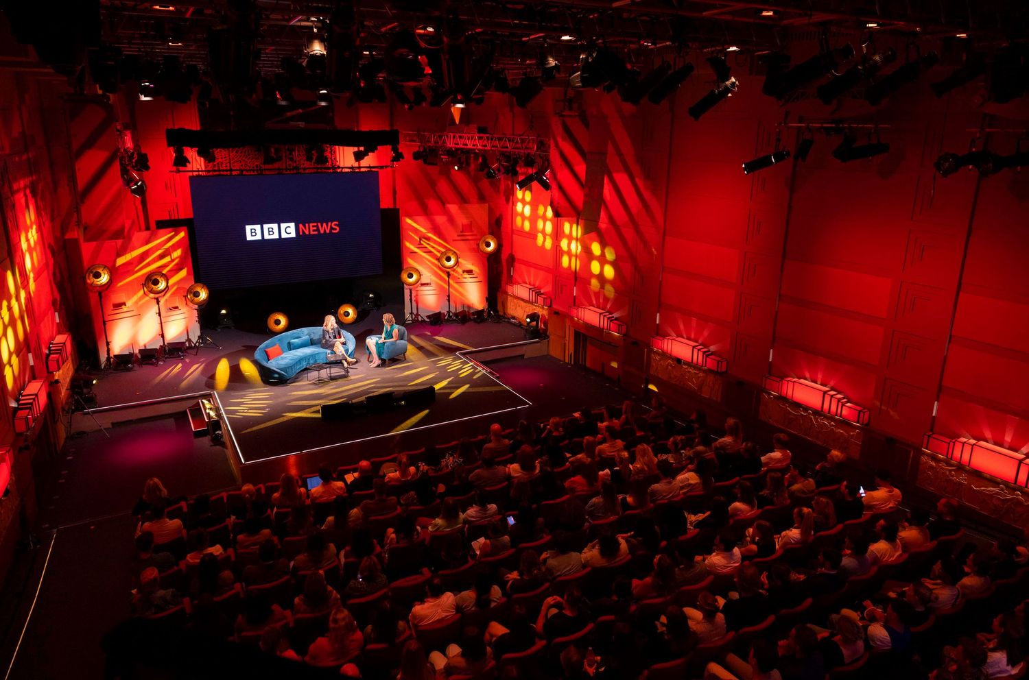 Concert venue with dramatic red lighting and large audience viewed from above. London Event Photographer