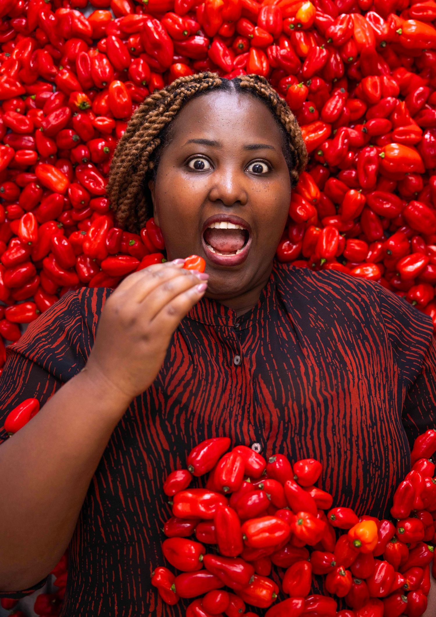 Person in striped outfit poses expressively against vibrant background of red peppers. London Event Photographer