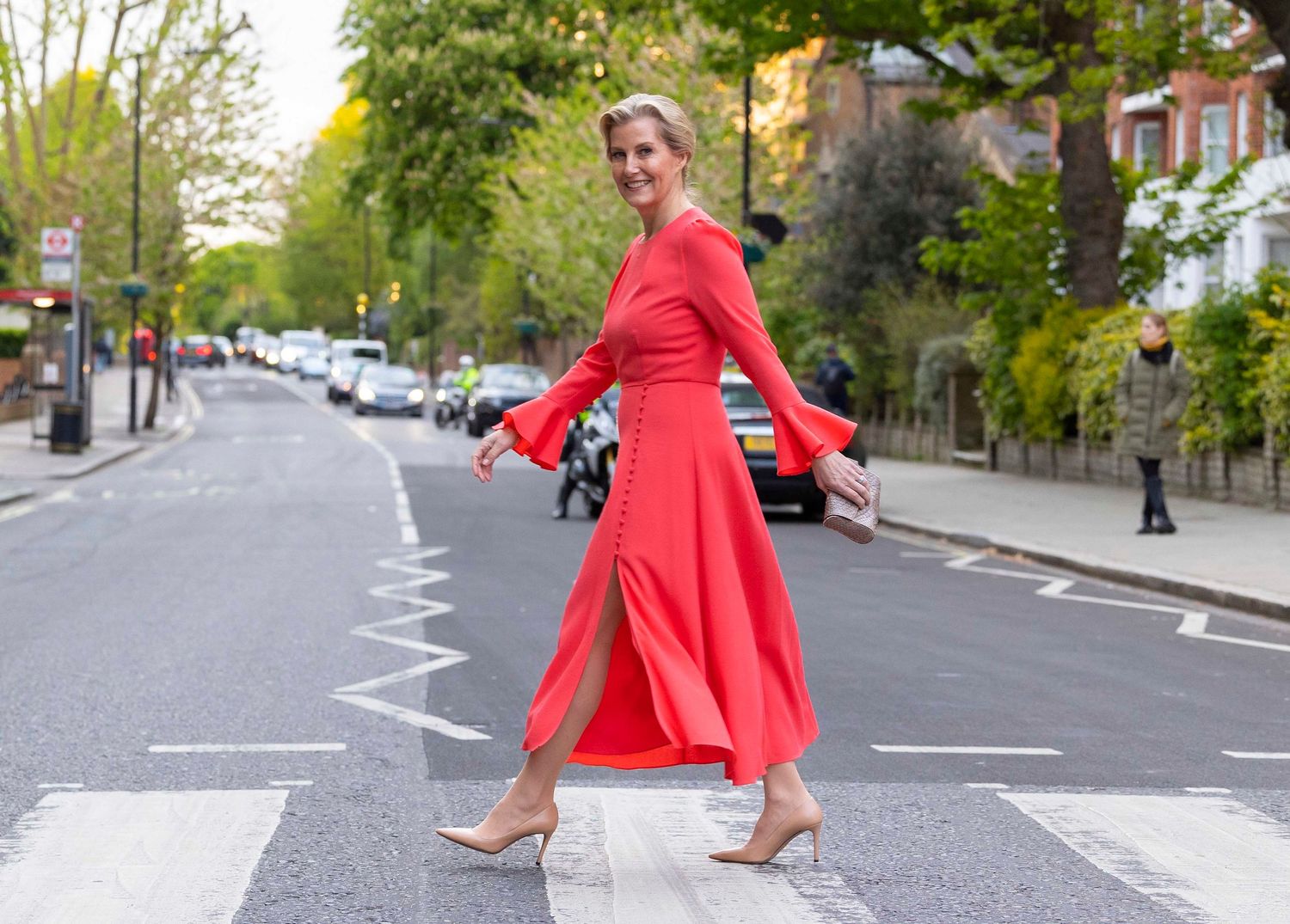 Woman in bright red jacket walking down a tree-lined urban street. London Event Photographer