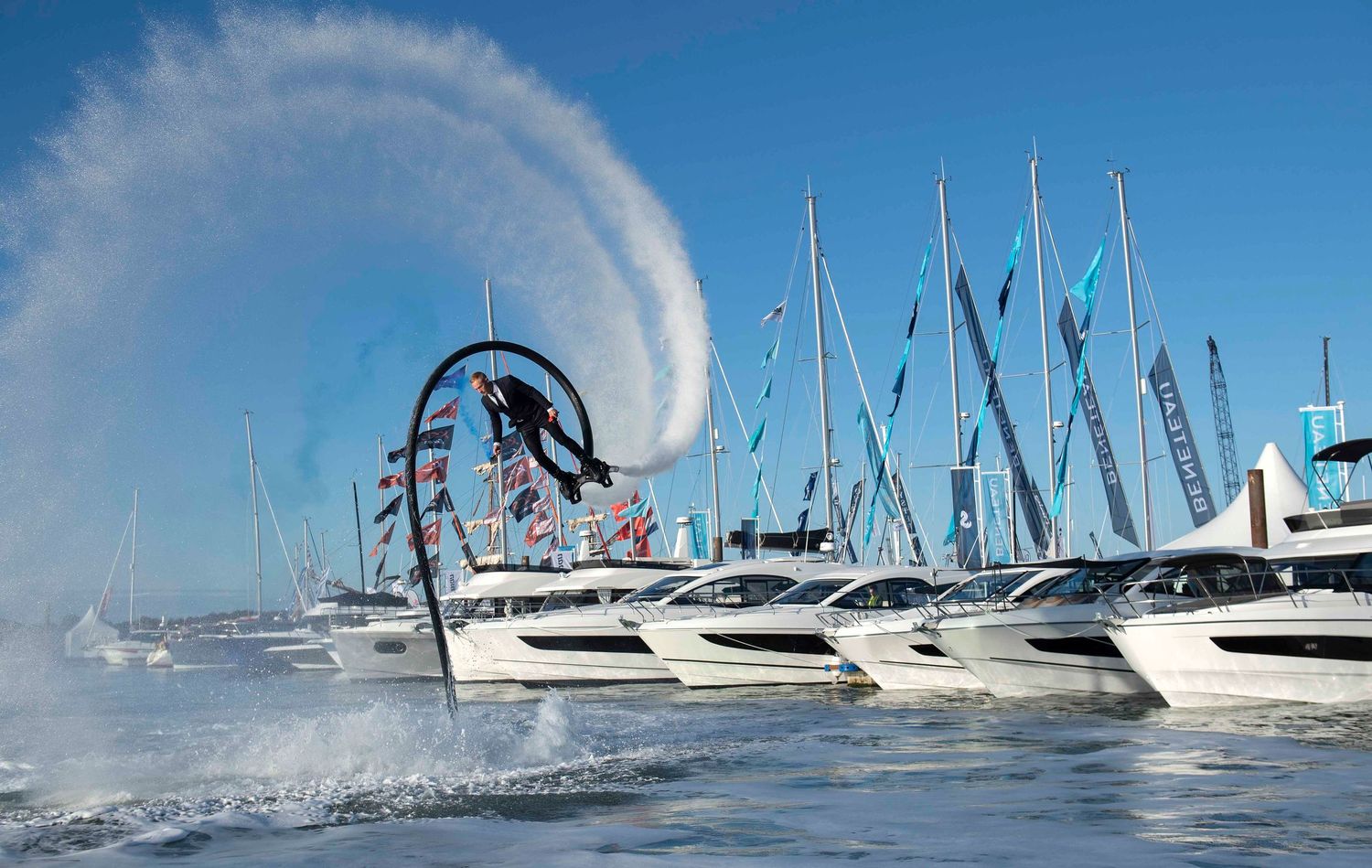 Sailing boats in formation creating dramatic water spray patterns against blue sky. London Event Photographer