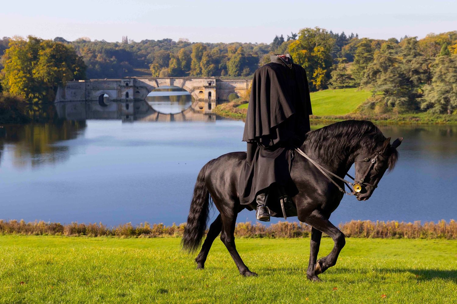 Black horses galloping gracefully across a green field near a lake on a sunny day. London Event Photographer