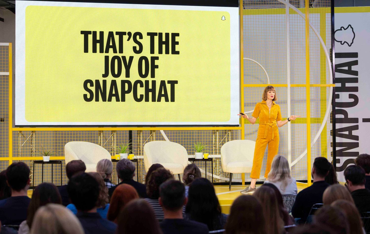 Conference presentation stage with bright yellow backdrop displaying text and multiple screens. London Event Photographer