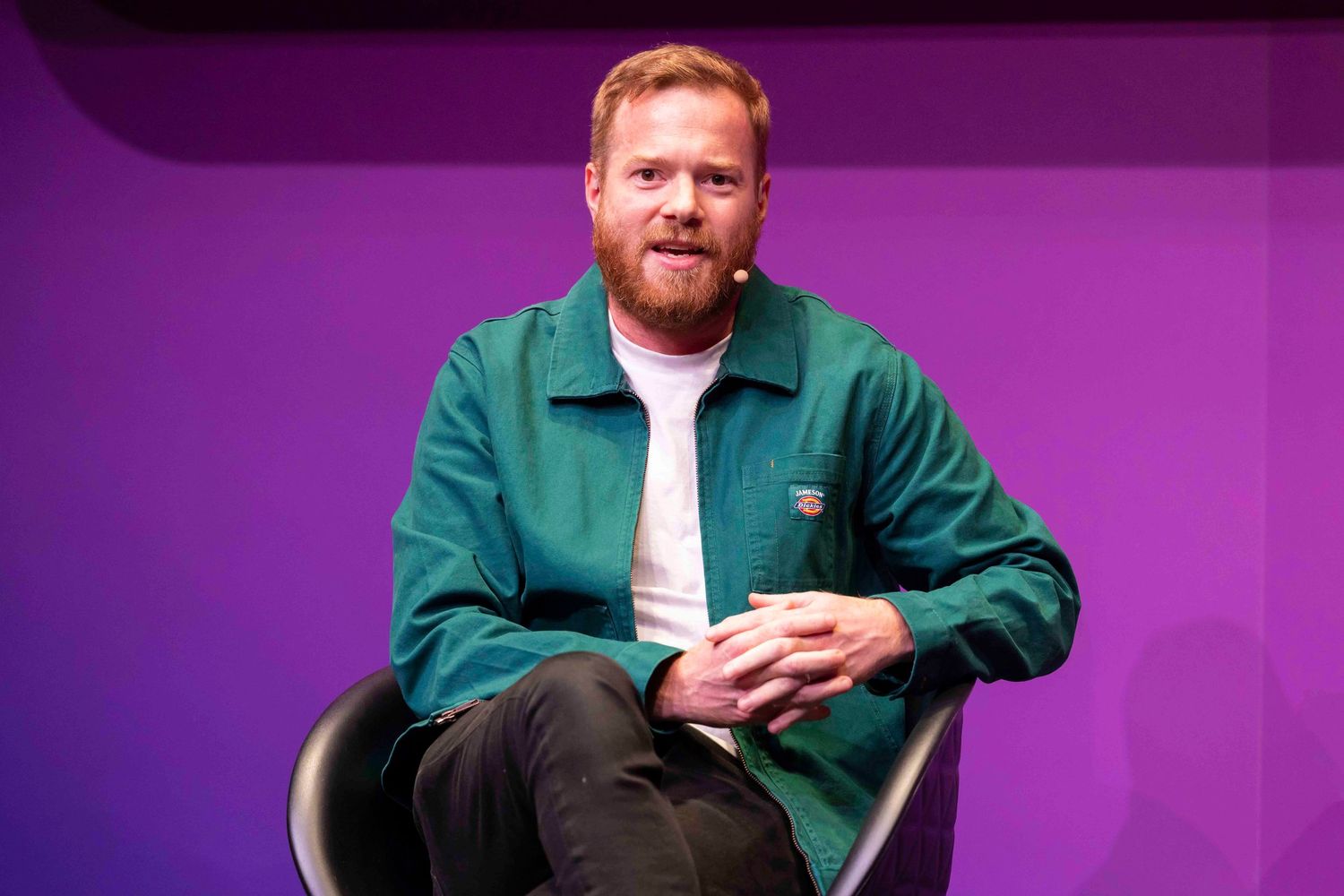 Speakers seated in casual conversation on stage with purple backdrop. London Event Photographer