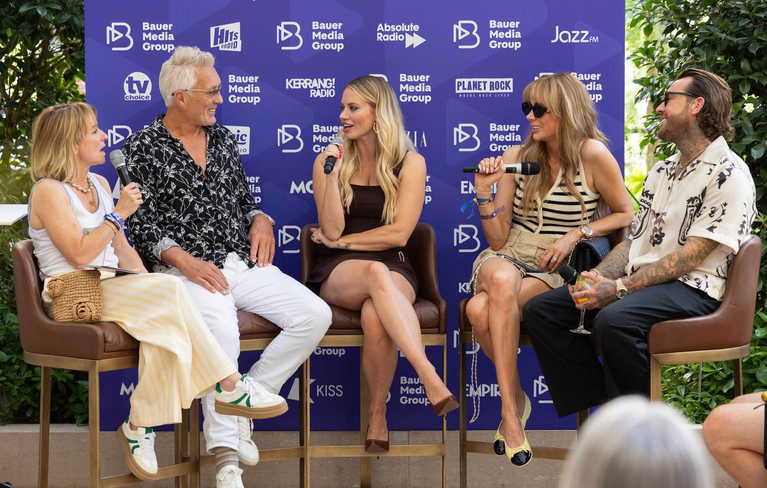 Panel discussion group seated outdoors against blue branded backdrop at media event. London Event Photographer